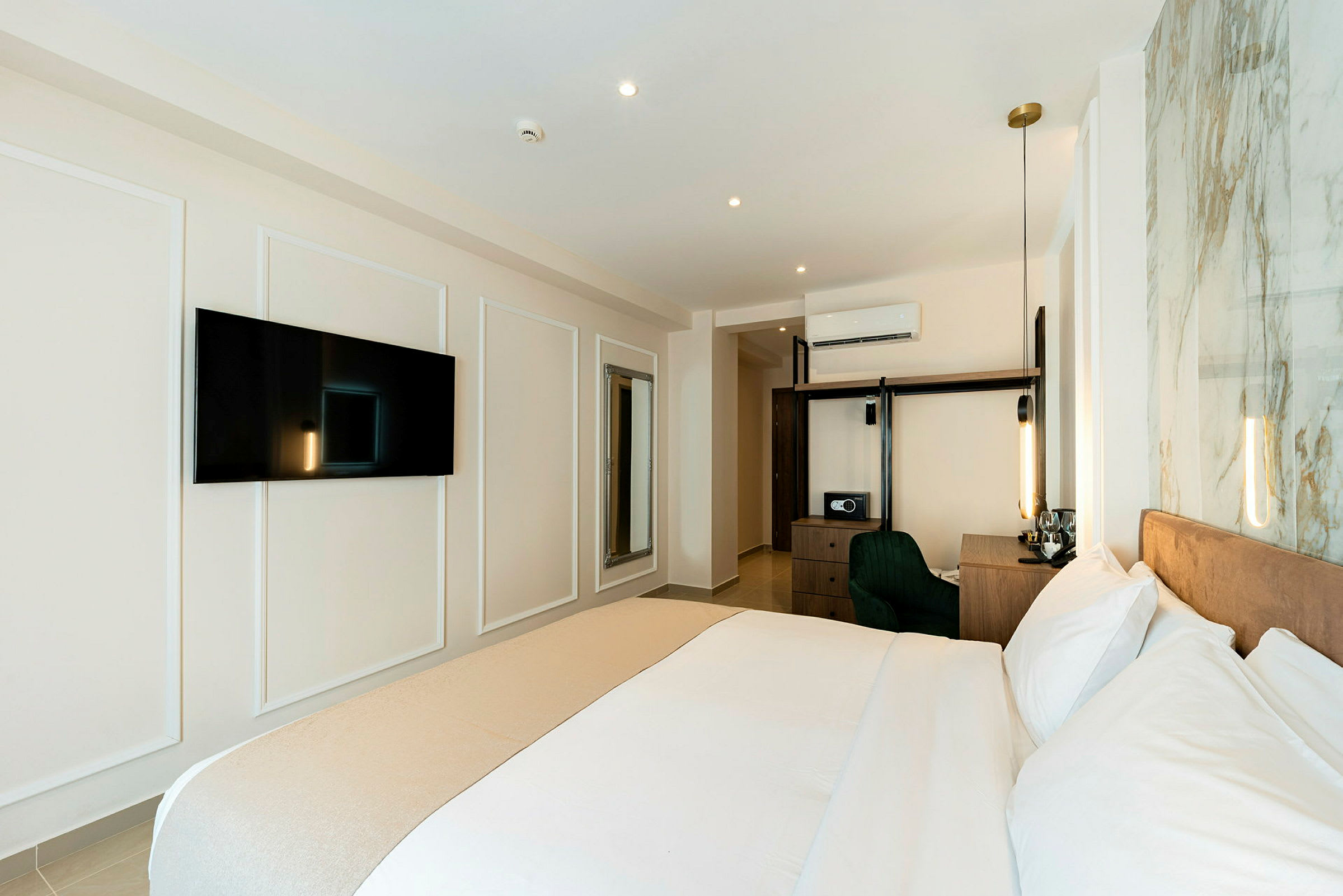 Ett modernt hotellrum med en stor säng, tv på väggen, skrivbord och förvaringsmöbler. (AI-genererad text)