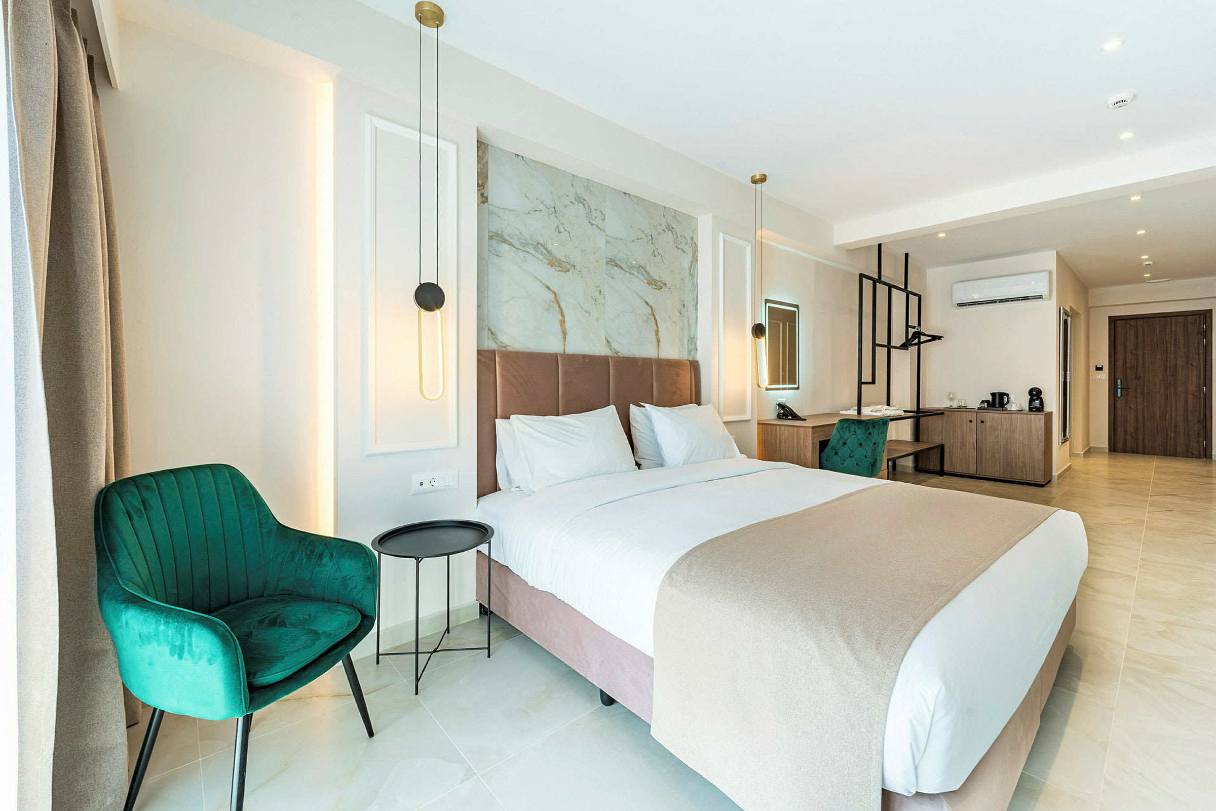Ett modernt hotellrum med en stor säng, gröna stolar och ett skrivbord. Rummet är välbelyst med vägglampor och har en stilren inredning. (AI-genererad text)