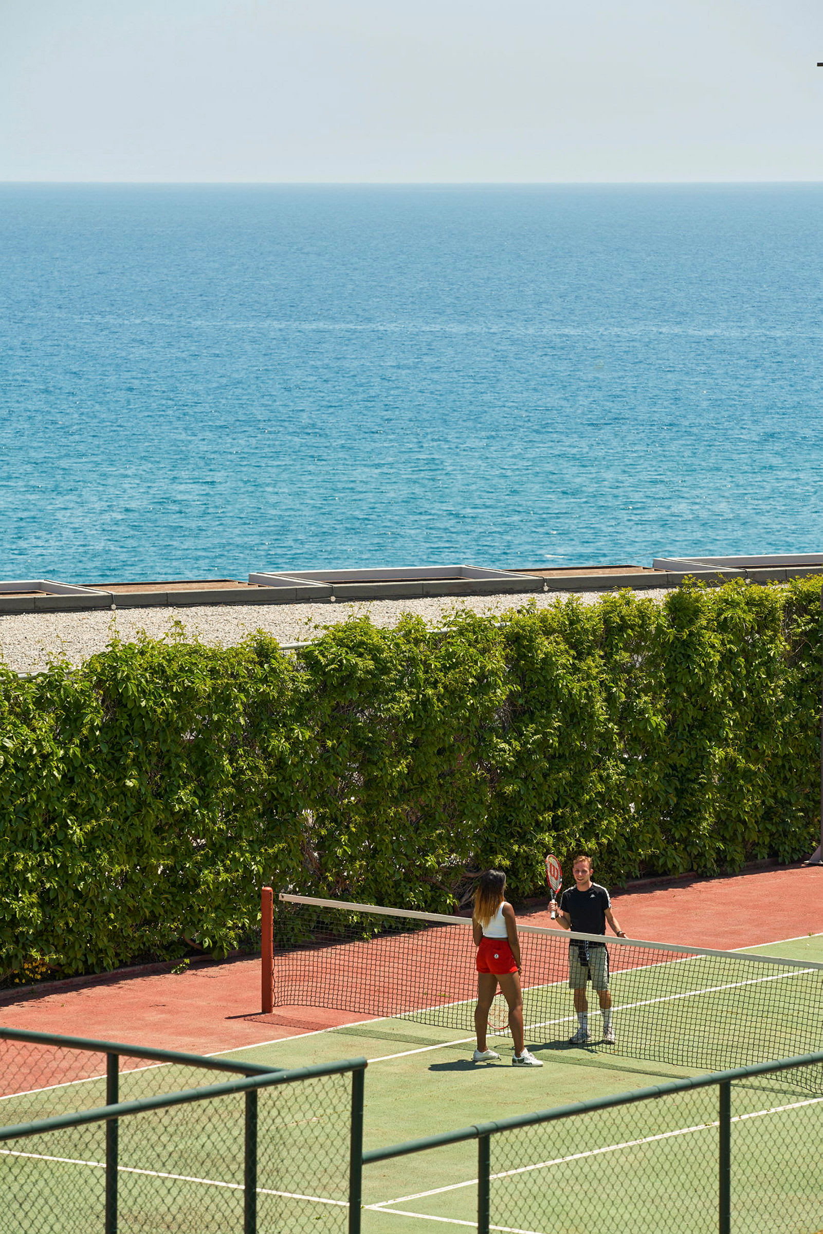Två personer spelar tennis på en tennisbana nära havet. (AI-genererad text)