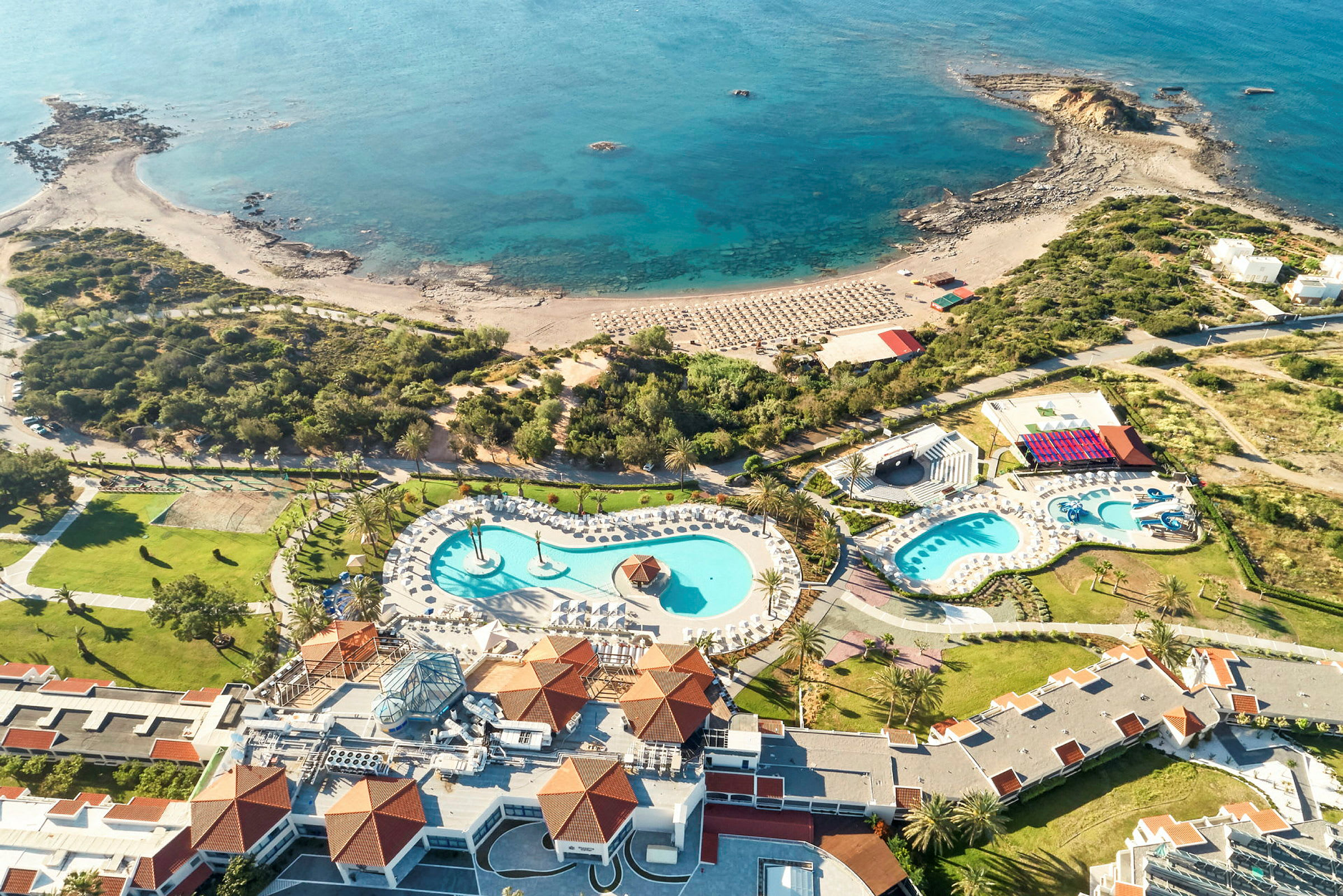 Flygfoto av ett semesterresort med poolområde och strand vid havet. (AI-genererad text)