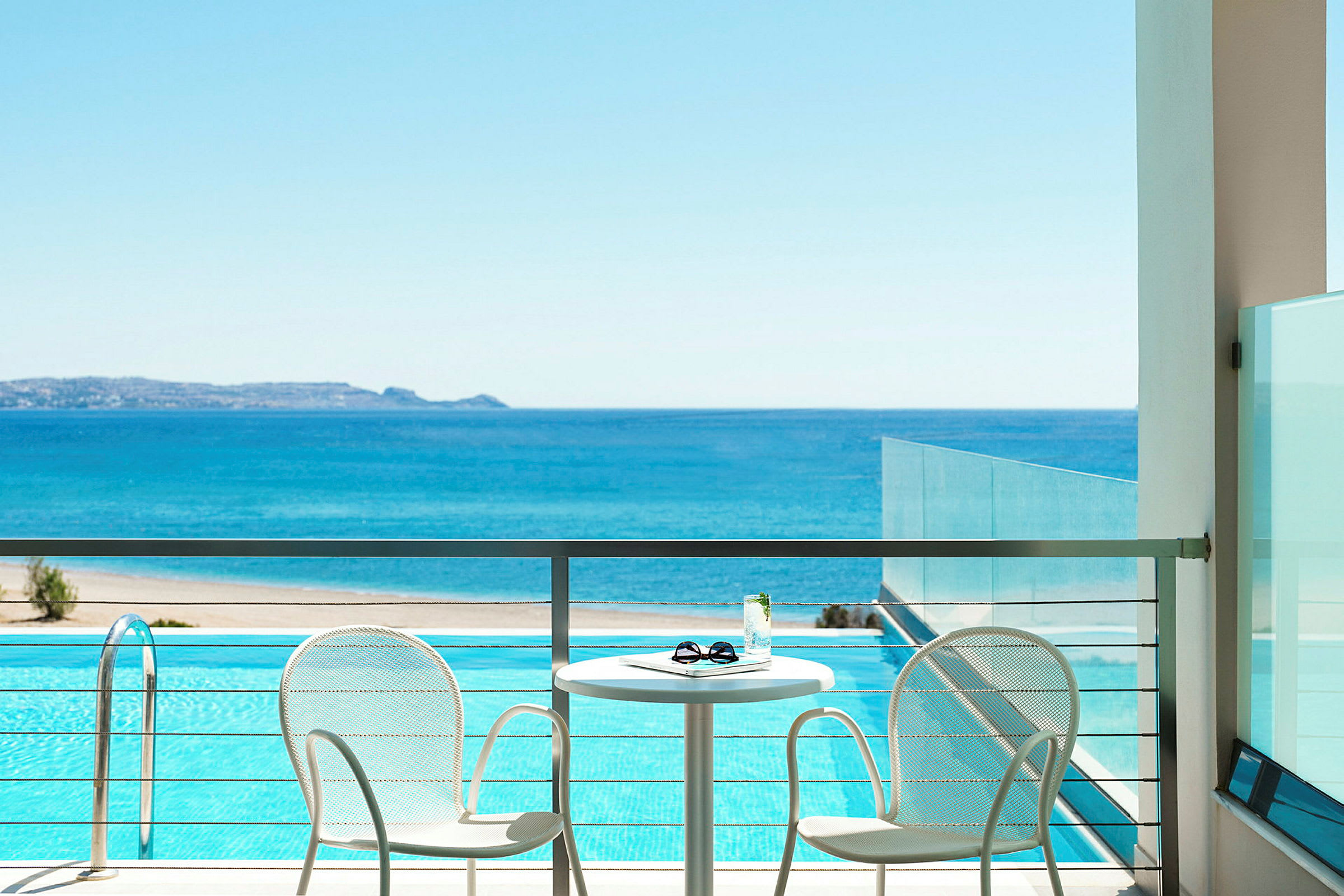 Terrass med två stolar och ett bord med utsikt över havet och en pool. (AI-genererad text)