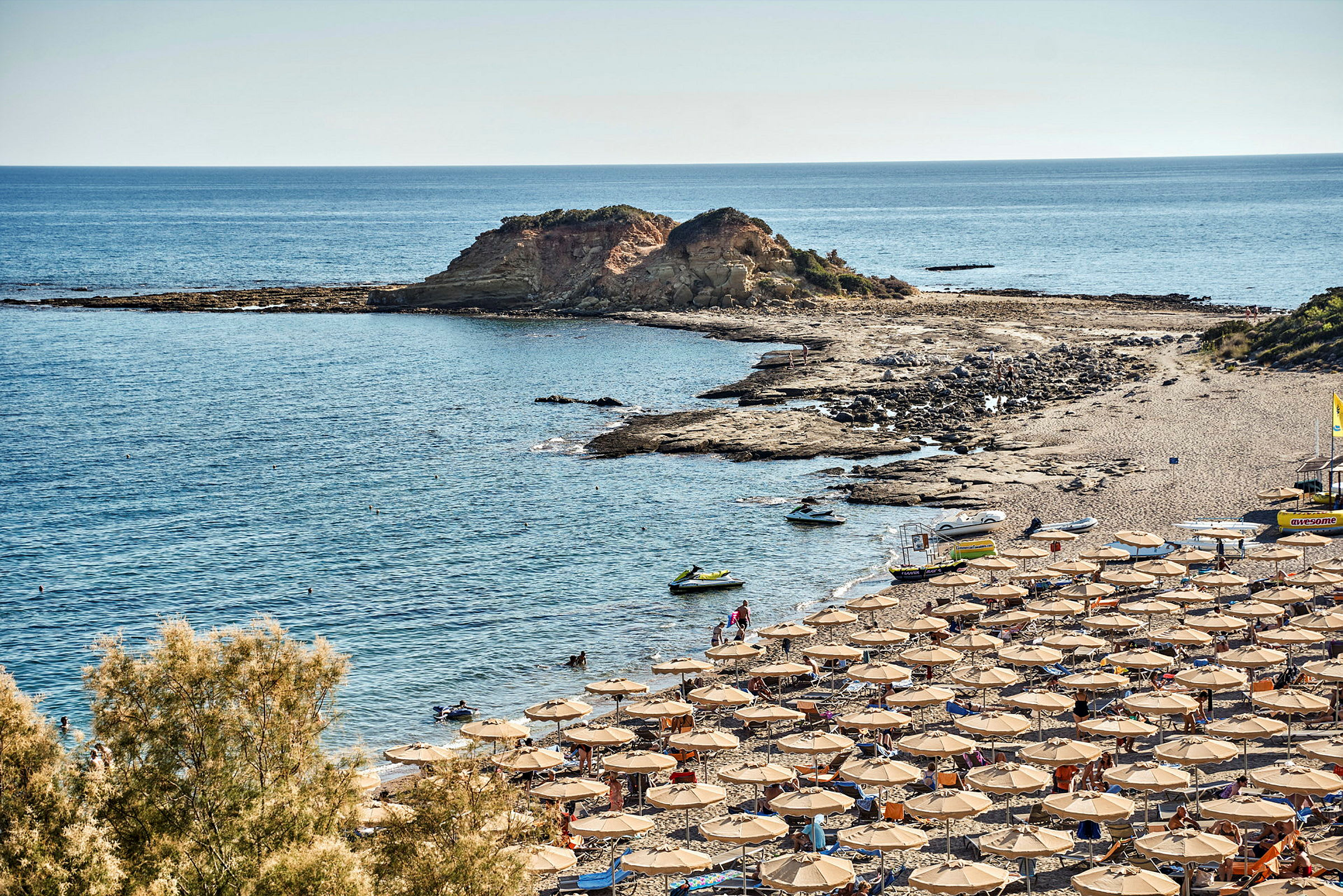 Solsängar och parasoller på en strand vid kusten med klippor och hav. (AI-genererad text)