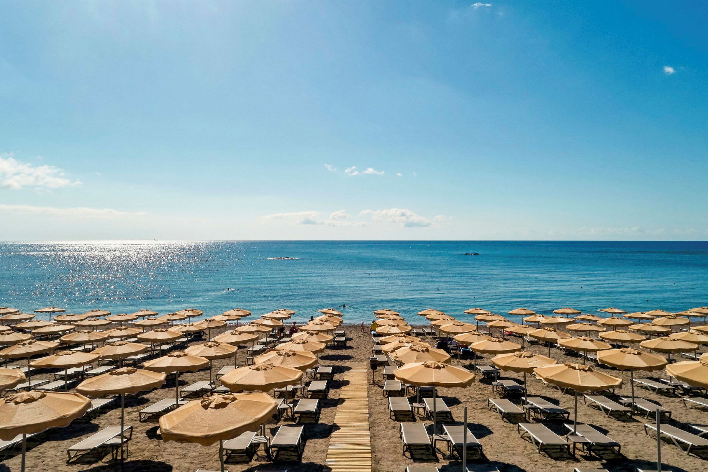 Strand med solstolar och parasoll, havet i bakgrunden. (AI-genererad text)