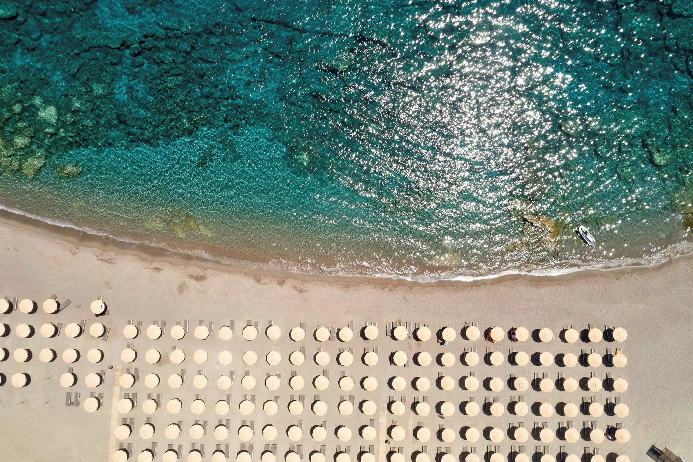 Strand med parasoller sedd från ovan nära klart vatten. (AI-genererad text)