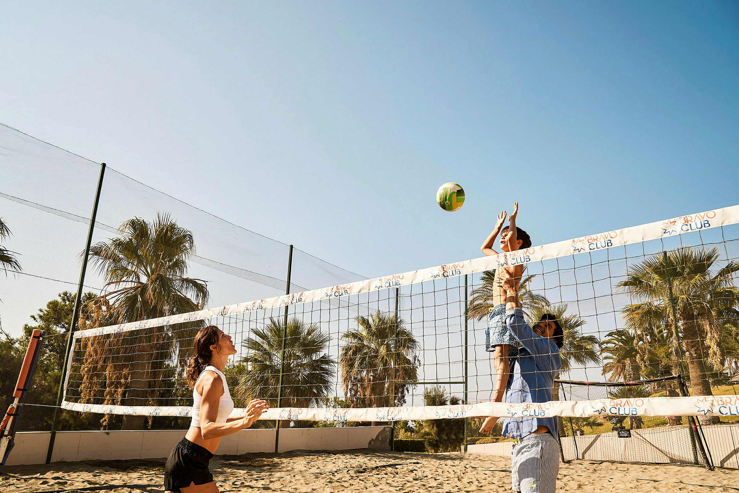 Personer spelar volleyboll på en sandplan med palmer i bakgrunden. (AI-genererad text)