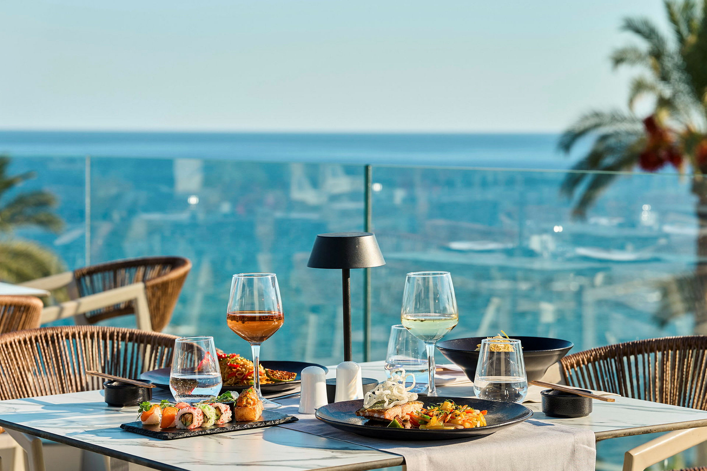 En dukad bord med mat och dryck på en terrass med utsikt över havet. (AI-genererad text)