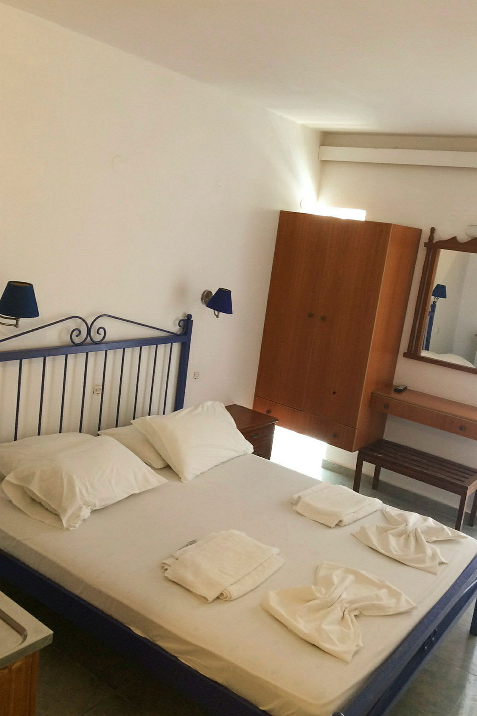 Ett hotellrum med en säng med vita sängkläder, handdukar arrangerade på sängen och möbler som inkluderar garderob och spegel. (AI-genererad text)