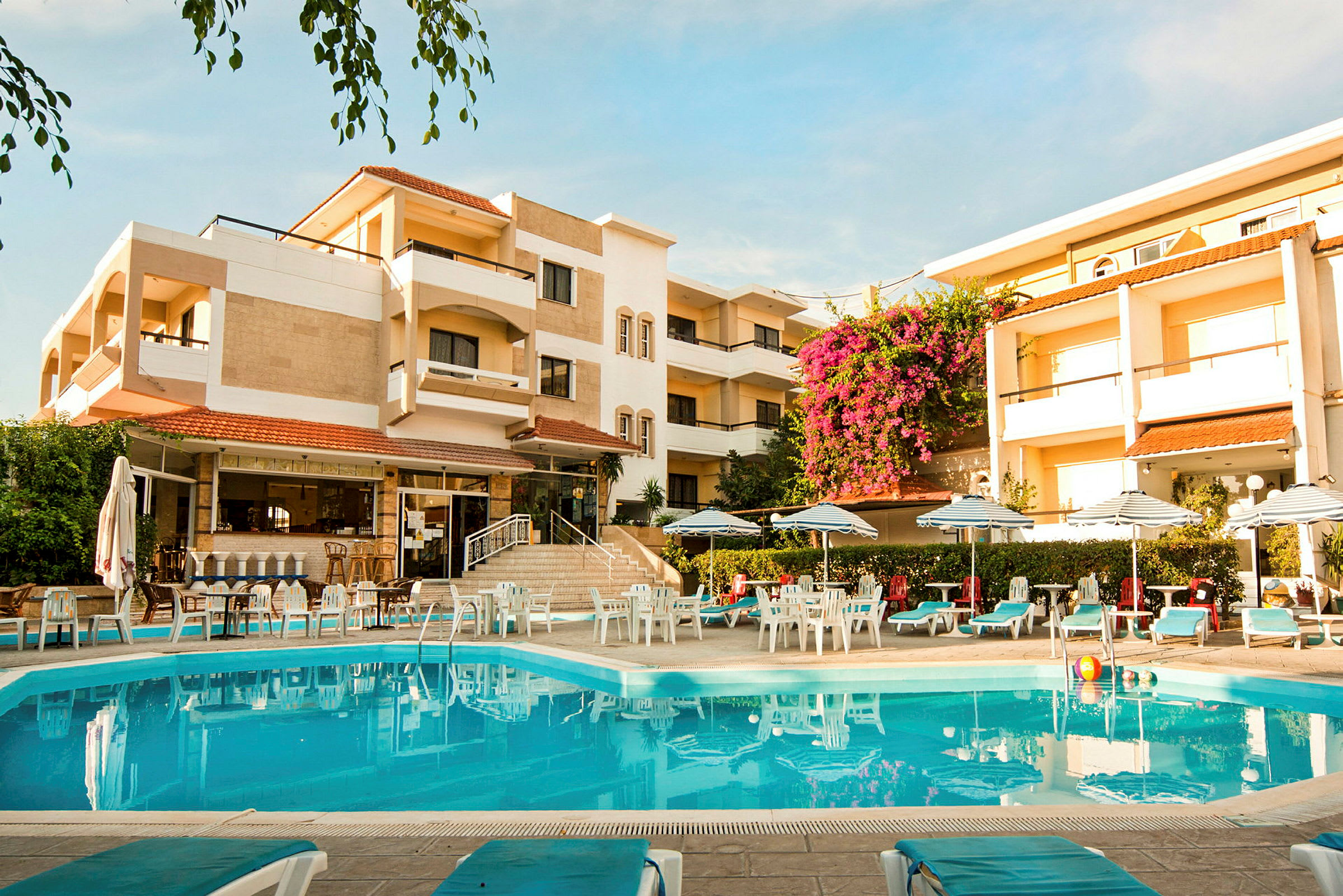 Hotellbyggnad med en pool i förgrunden och omgiven av solstolar och parasoller. (AI-genererad text)