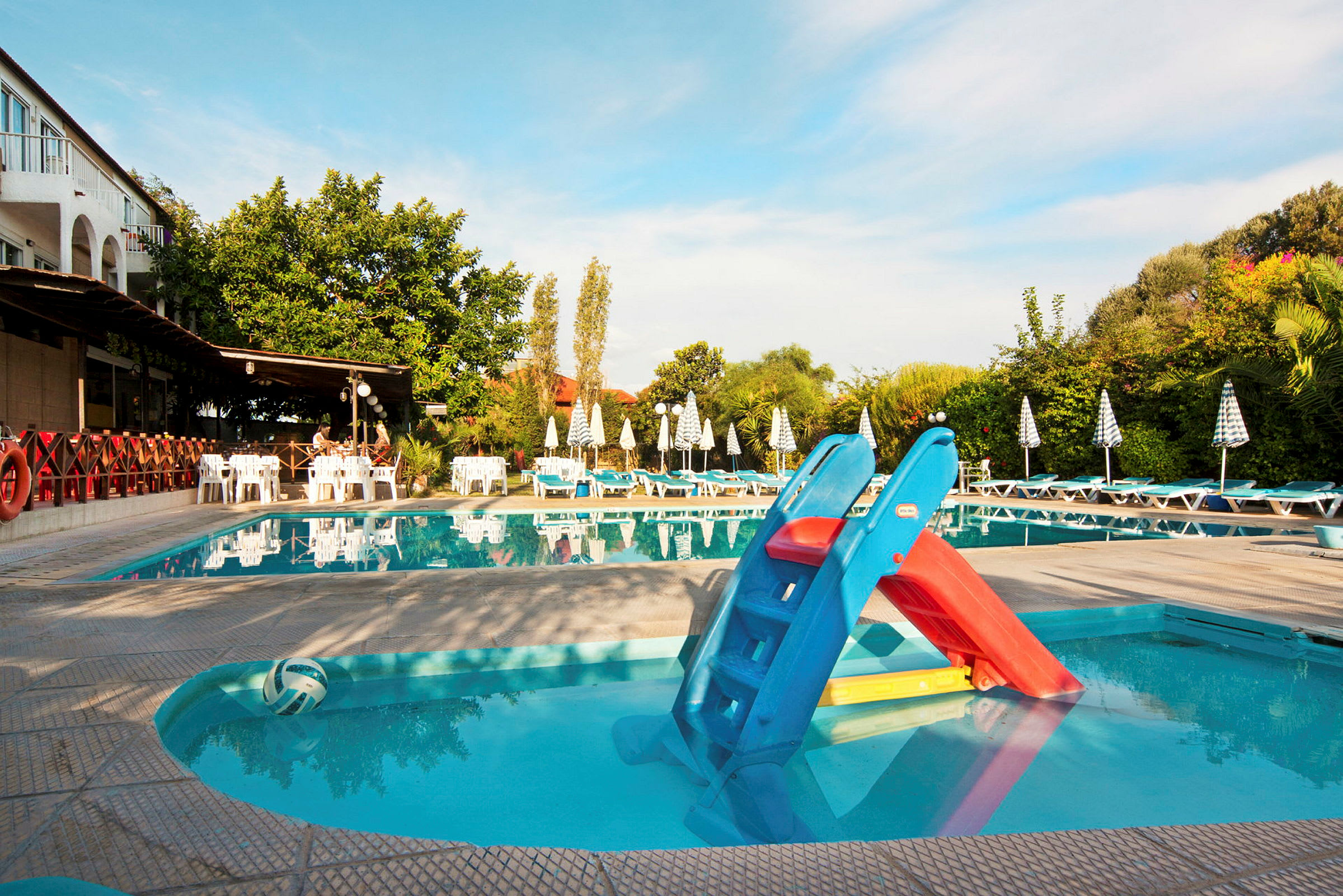 Bild av en swimmingpool med solstolar och parasoller runt. En liten vattenrutschbana är placerad vid poolkanten. (AI-genererad text)