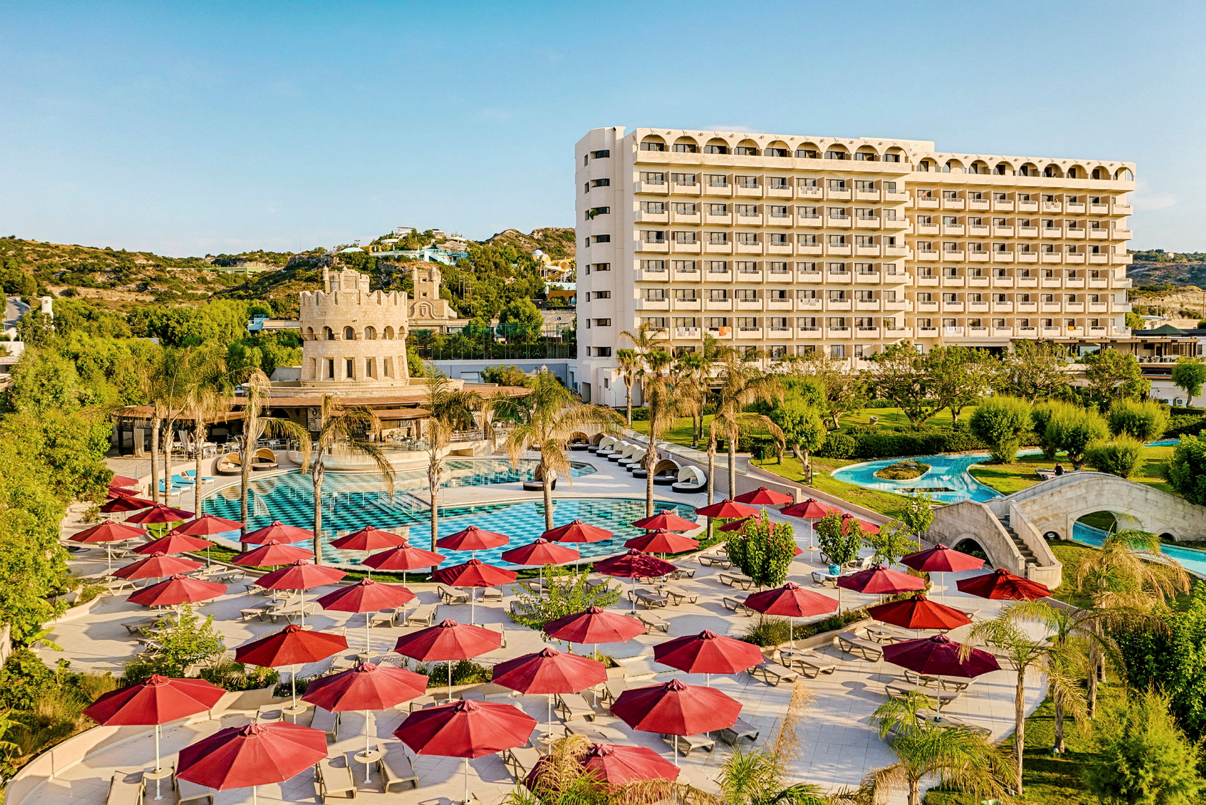 Hotellområde med pool, solstolar, röda parasoller och en större byggnad i bakgrunden. (AI-genererad text)
