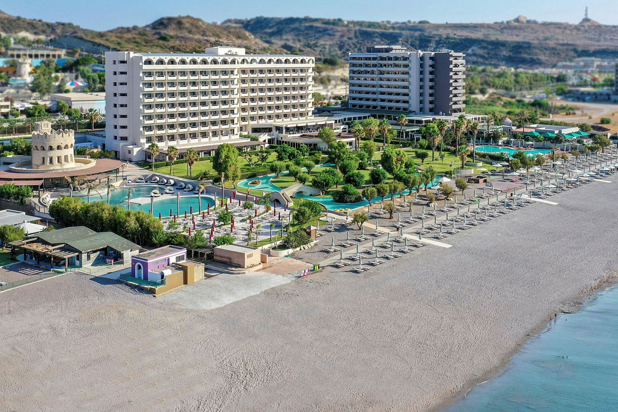 En strand med parasoller och solstolar, samt hotell och poolområden i bakgrunden. (AI-genererad text)
