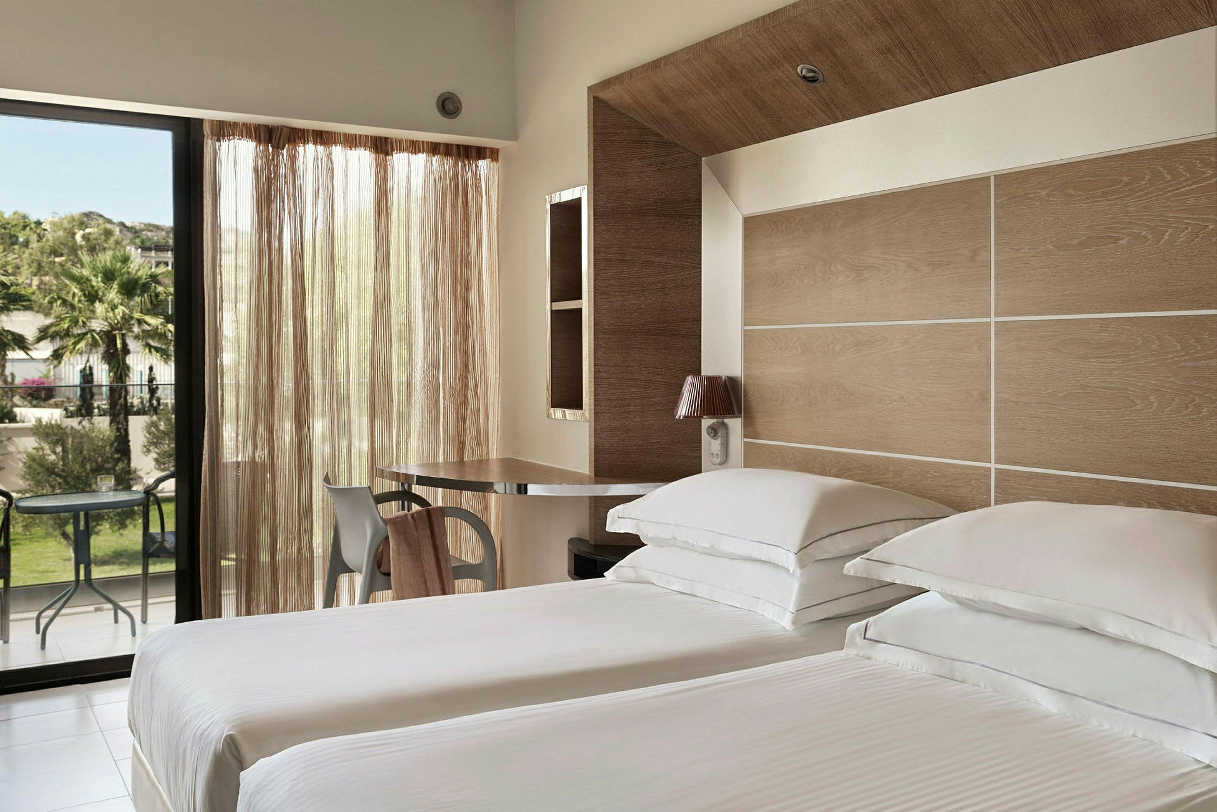 Ett hotellrum med två enkelsängar, en modern design, ett skrivbord och stora fönster med utsikt mot en grönskande trädgård. (AI-genererad text)