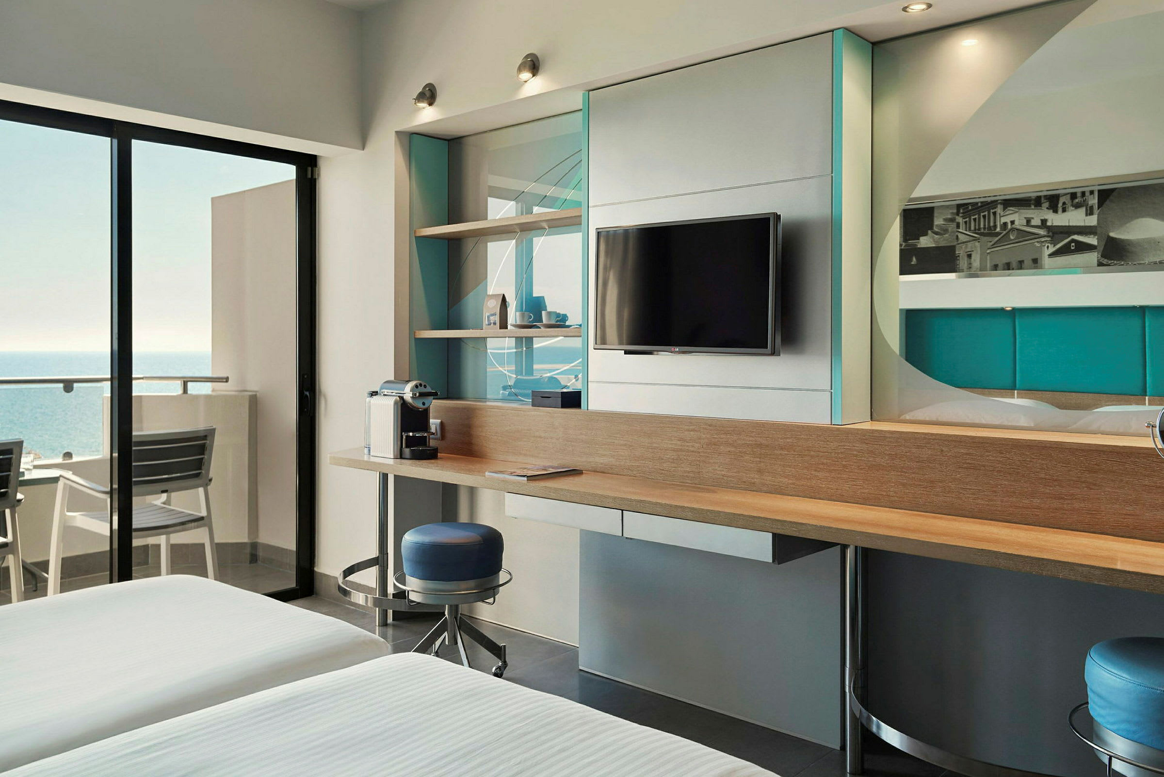 Ett modernt hotellrum med havsutsikt, en TV på väggen och en kaffebryggare på ett skrivbord. (AI-genererad text)