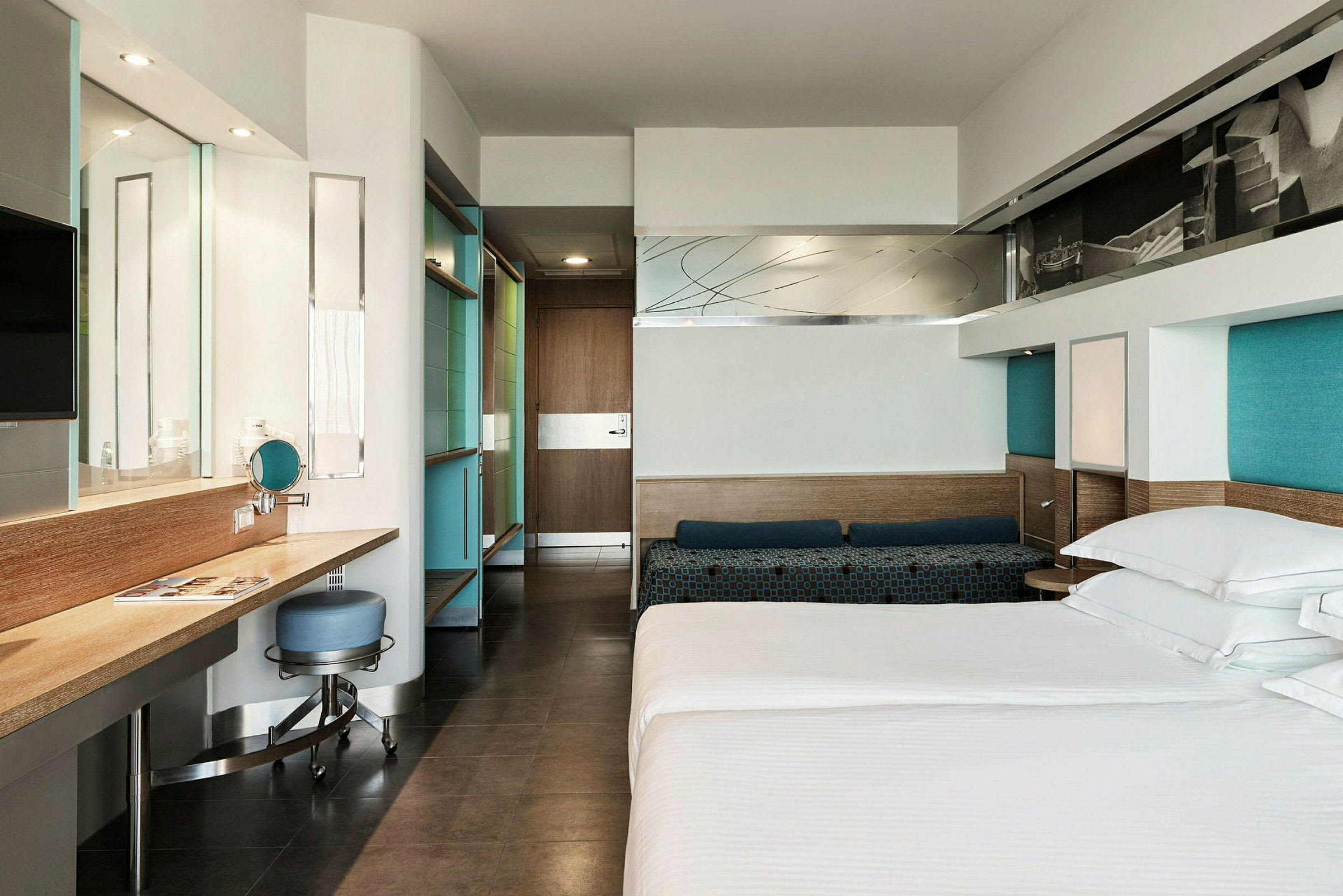 Ett modernt hotellrum med en säng, skrivbord och stol samt spegel och garderob. (AI-genererad text)