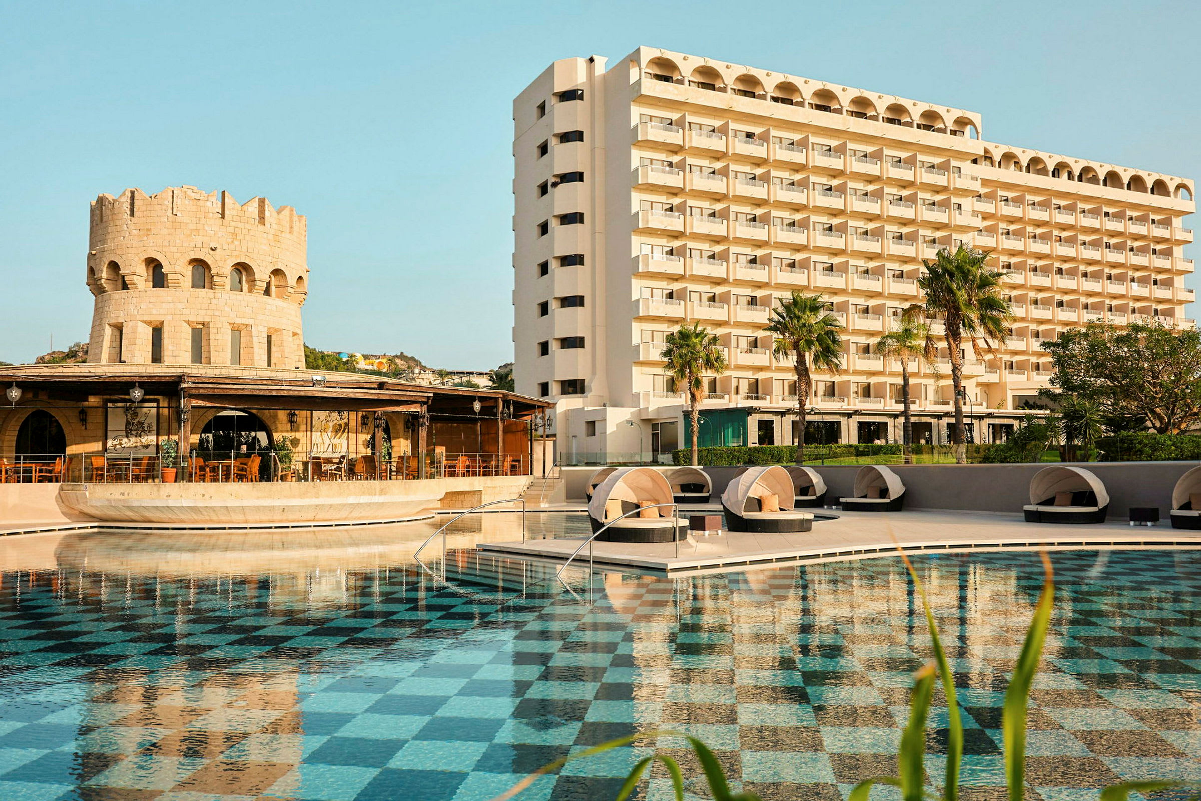 Hotellbyggnad med pool och solstolar. (AI-genererad text)