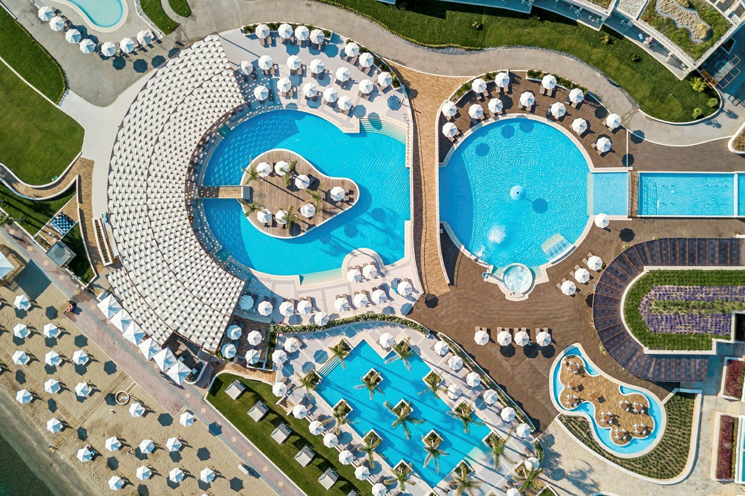 Flygfoto över ett hotellområde med flera pooler, solstolar och parasoller. (AI-genererad text)