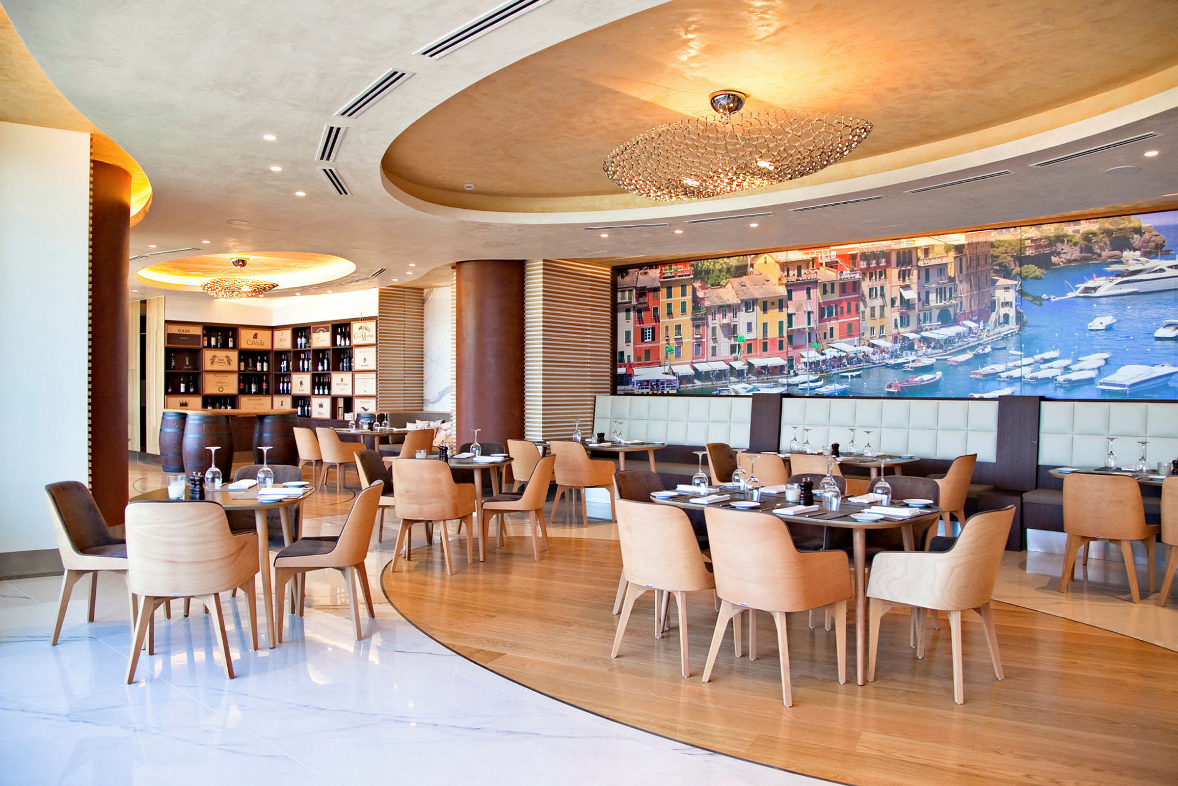 Interiör av en modern restaurang med träbord och stolar, en muralvägg föreställande en strandstad och en elegant taklampa. (AI-genererad text)