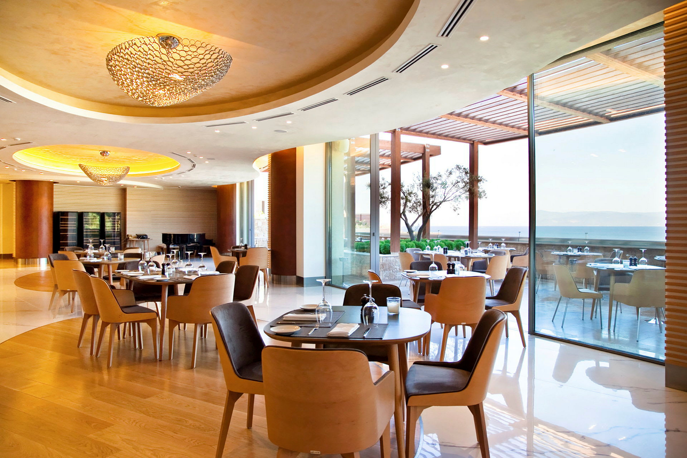 En rymlig restaurang med moderna möbler och stora fönster som vetter ut mot en terrass med havsutsikt. (AI-genererad text)