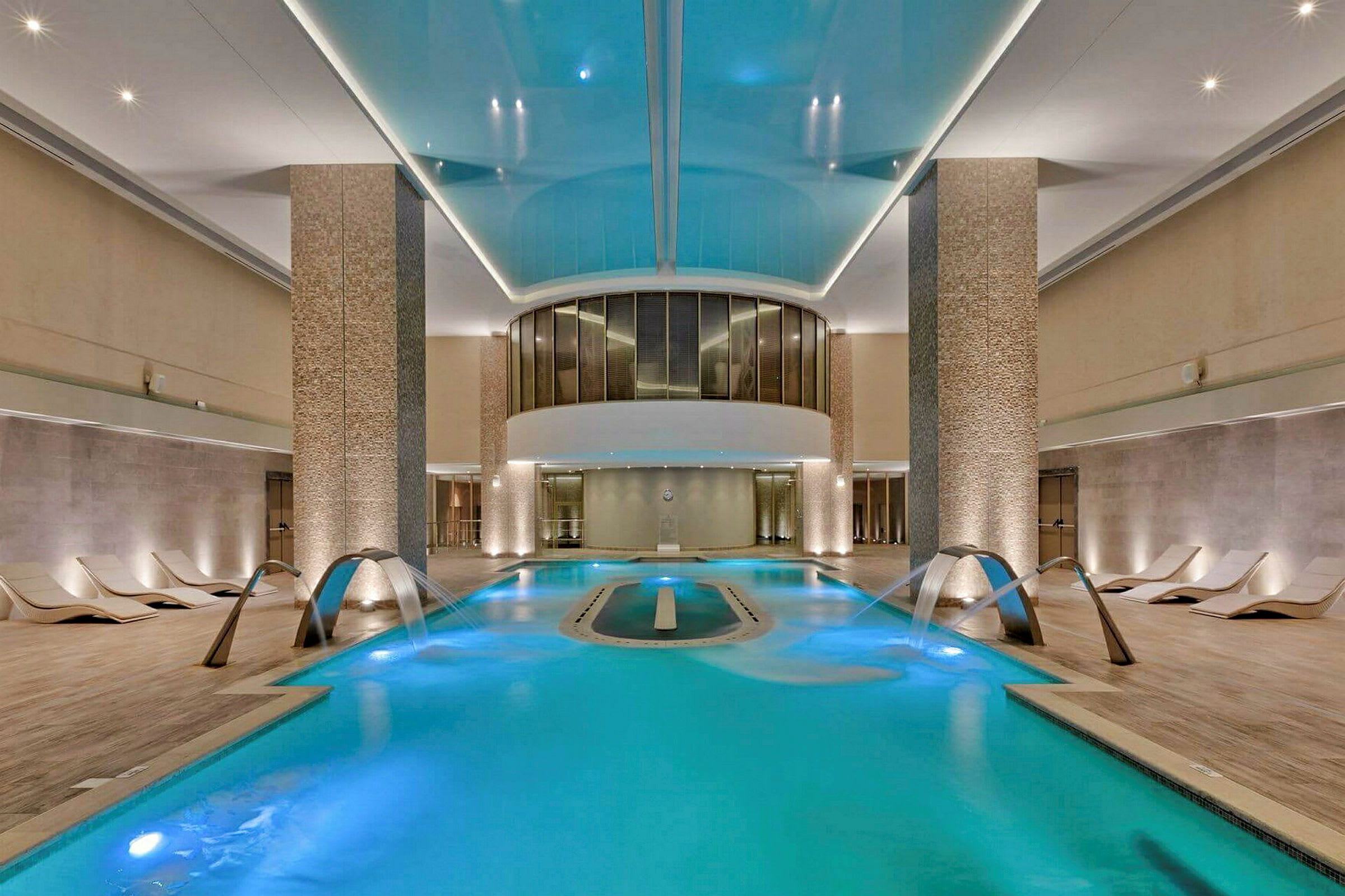 Ett modernt inomhusspa med en upplyst pool, vattenstrålar och bekväma solsängar vid sidorna. (AI-genererad text)