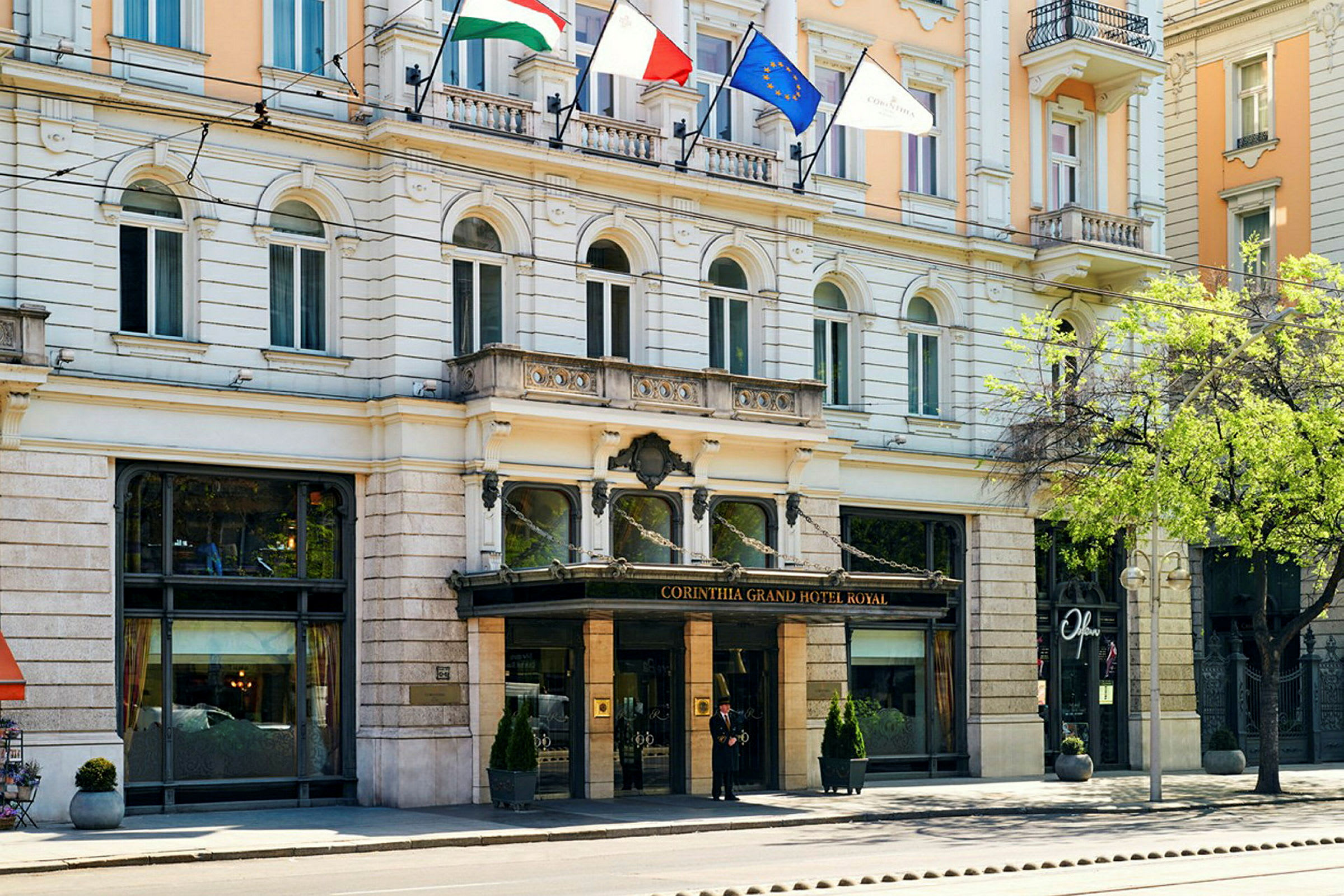 Framsidan av Corinthia Grand Hotel Royal med glasentré och flaggor ovanför. (AI-genererad text)