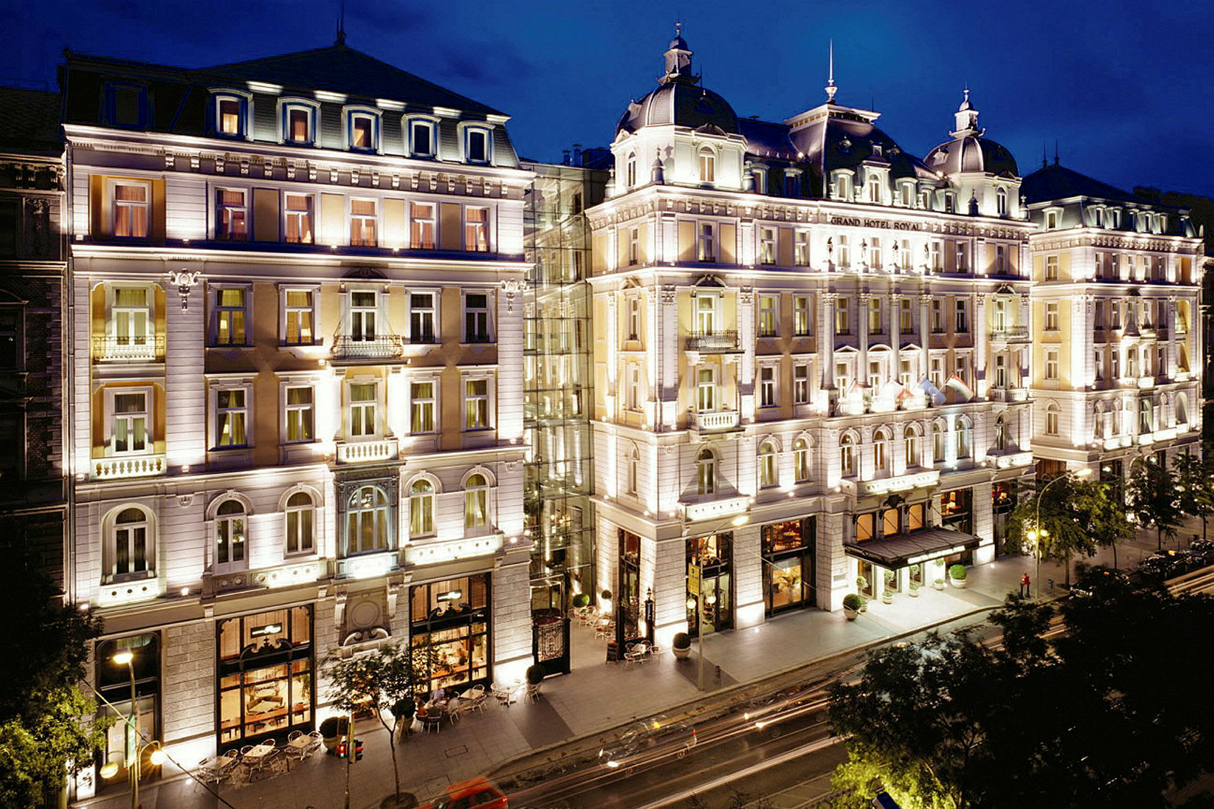 Upplyst hotellbyggnad i klassisk stil med flera våningar, fotad på kvällen. (AI-genererad text)