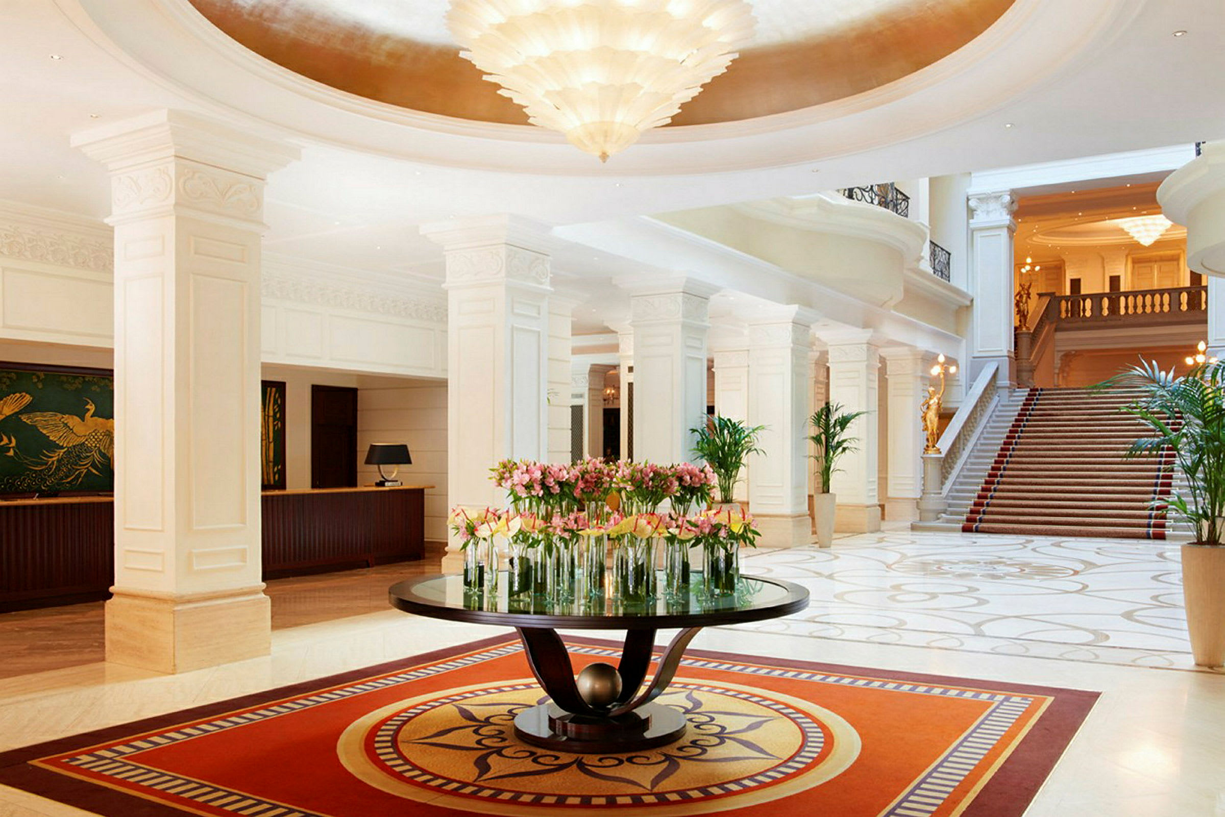 Ett elegant hotellobby med marmorgolv, en centerbord dekorerad med blommor och en trappa i bakgrunden. (AI-genererad text)