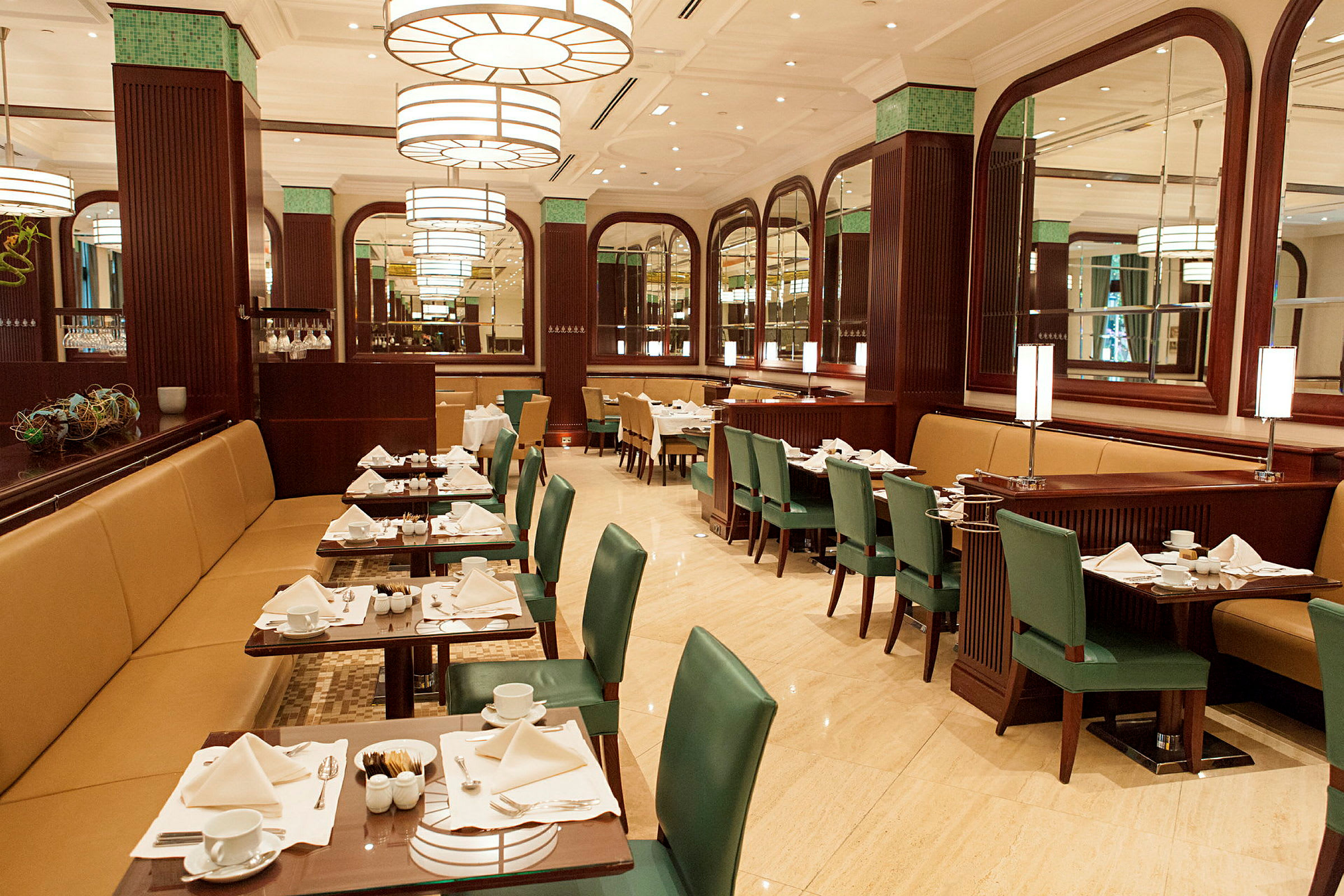 Restaurang med dukade bord, gröna stolar och stora speglar. (AI-genererad text)
