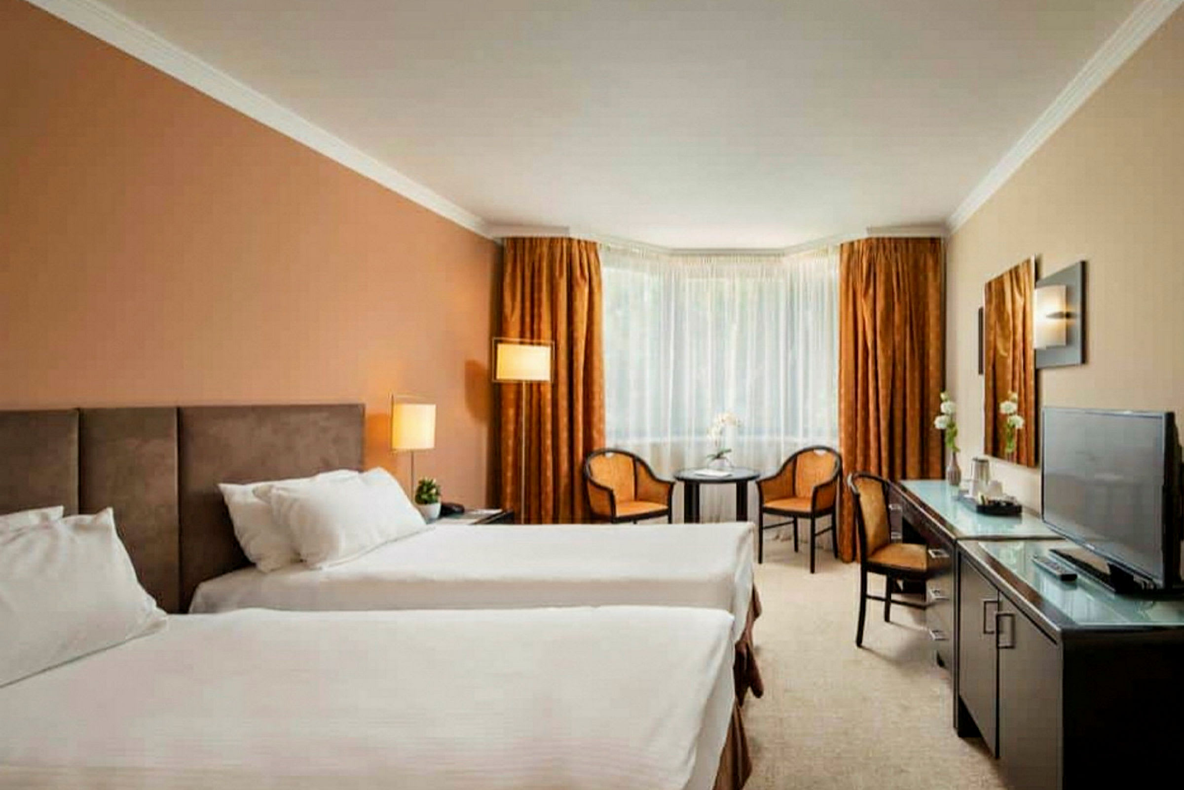 Hotellrum med två enkelsängar, ett bord, två stolar och en TV. (AI-genererad text)