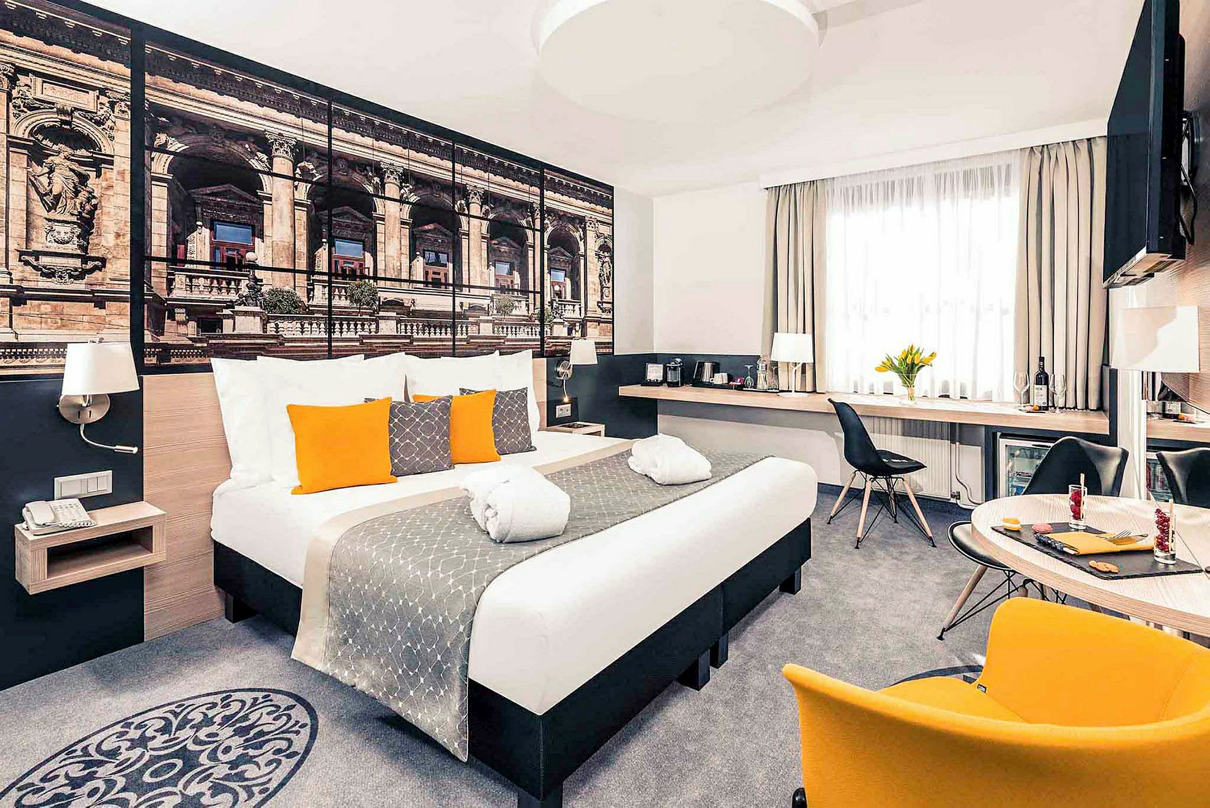 Modernt hotellrum med dubbelsäng, dekorativa kuddar, och en stor väggbild av arkitektur. (AI-genererad text)