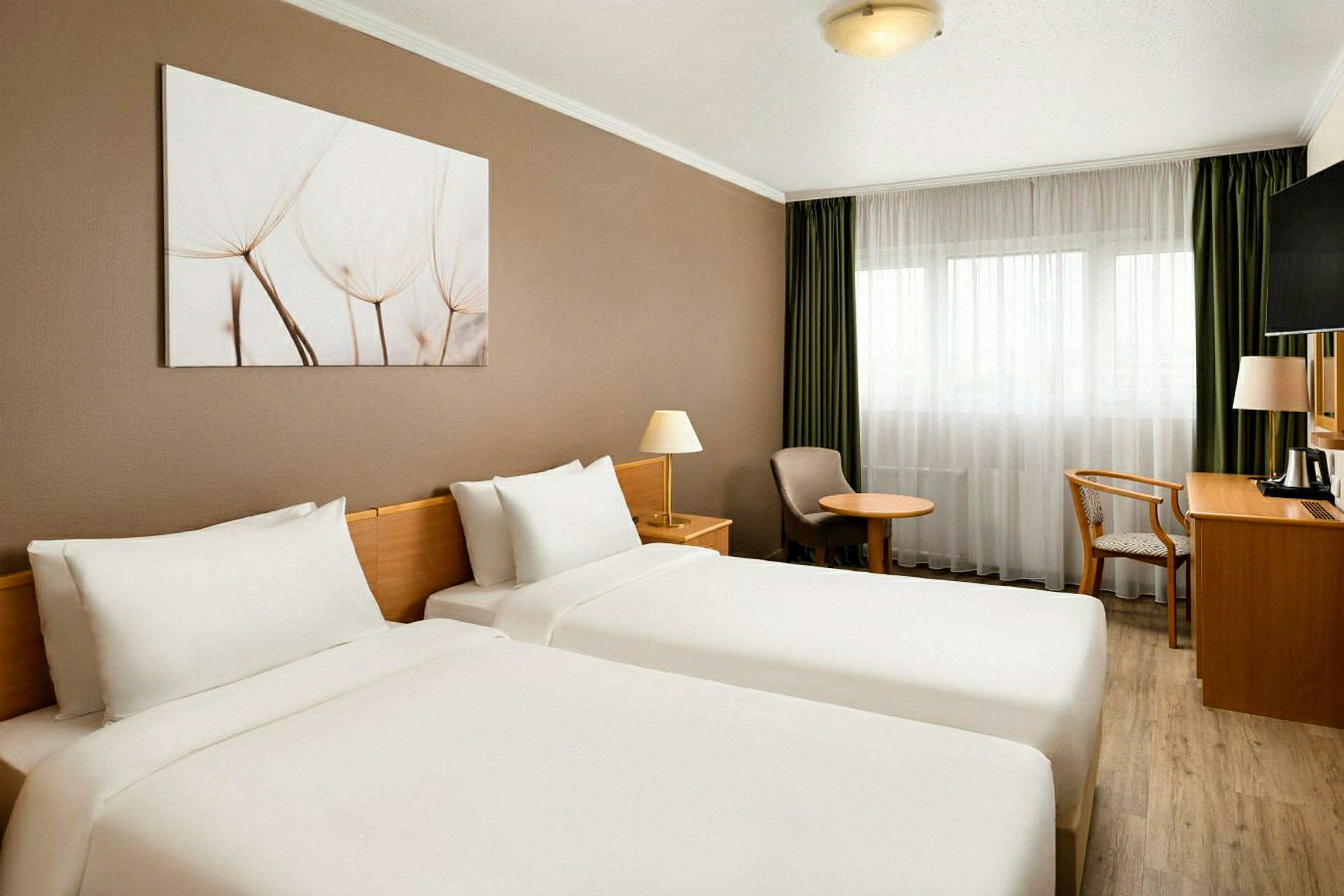 Ett hotellrum med två enkelsängar, vita sängkläder, en målning på väggen samt fönster med gröna gardiner. (AI-genererad text)
