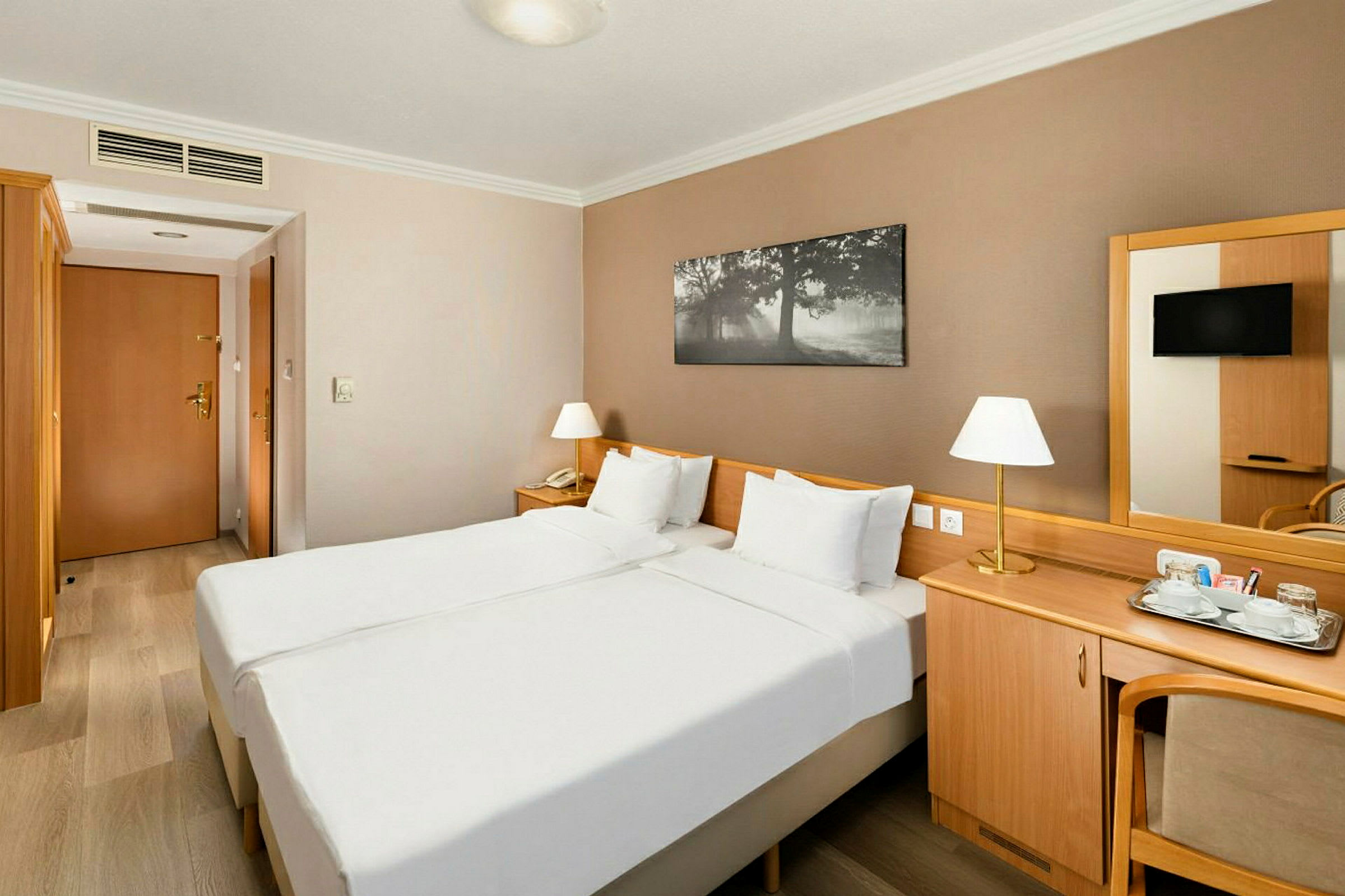 Bild av ett bekvämt hotellrum med två enkelsängar, en träskrivbord, spegel och lampor. (AI-genererad text)