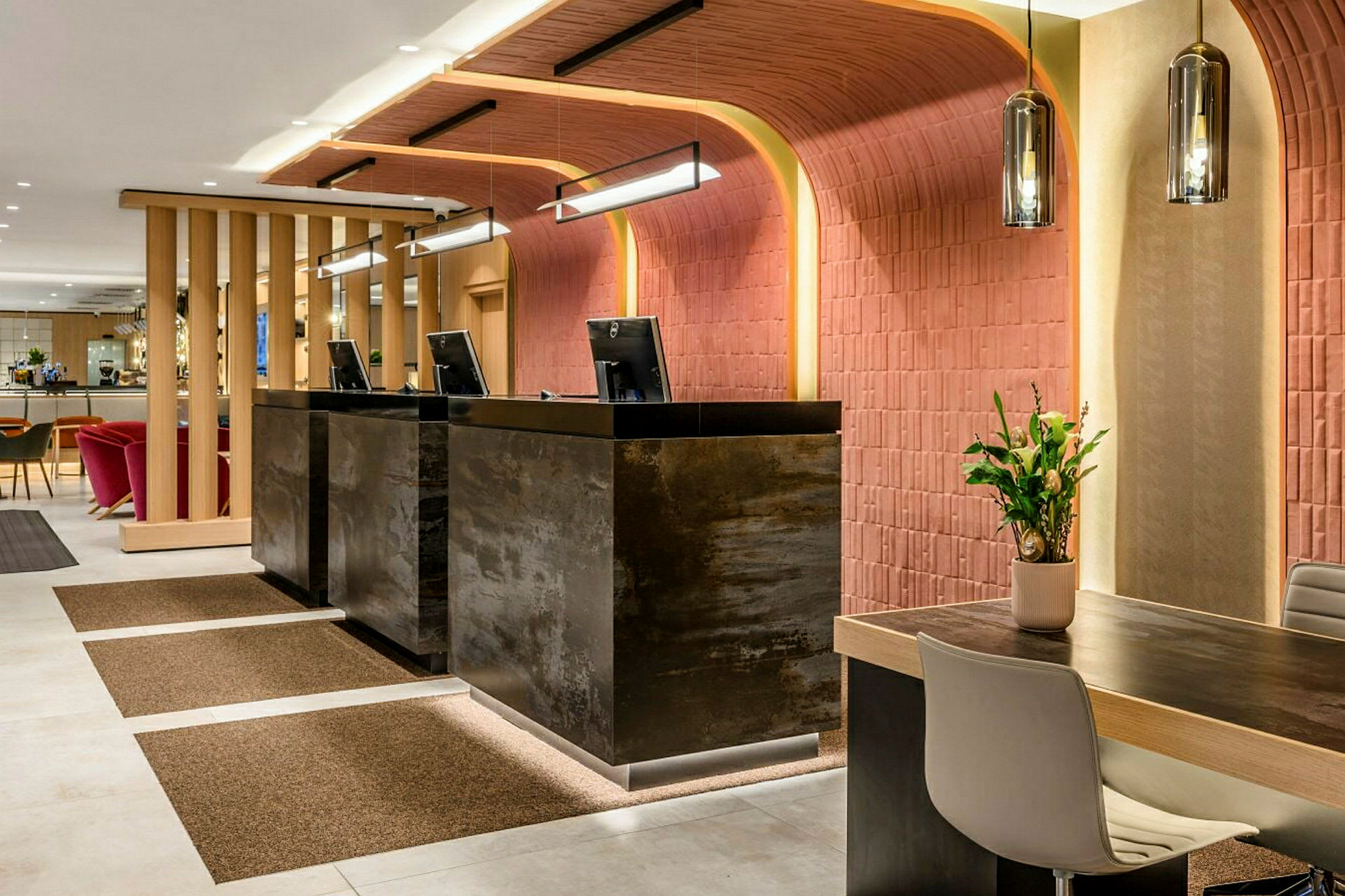 Receptionen av ett hotell med moderna möbler och inredning, tre diskar med dataskärmar samt en sittgrupp i bakgrunden. (AI-genererad text)