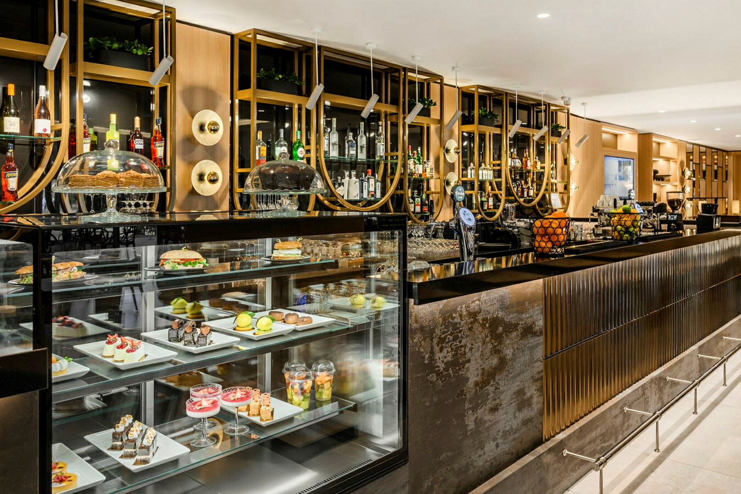 En elegant bardisk med inbyggda glasmontrar som visar olika desserter och frukter. Bakom baren syns hyllor med spritflaskor och dekorativa inslag. (AI-genererad text)