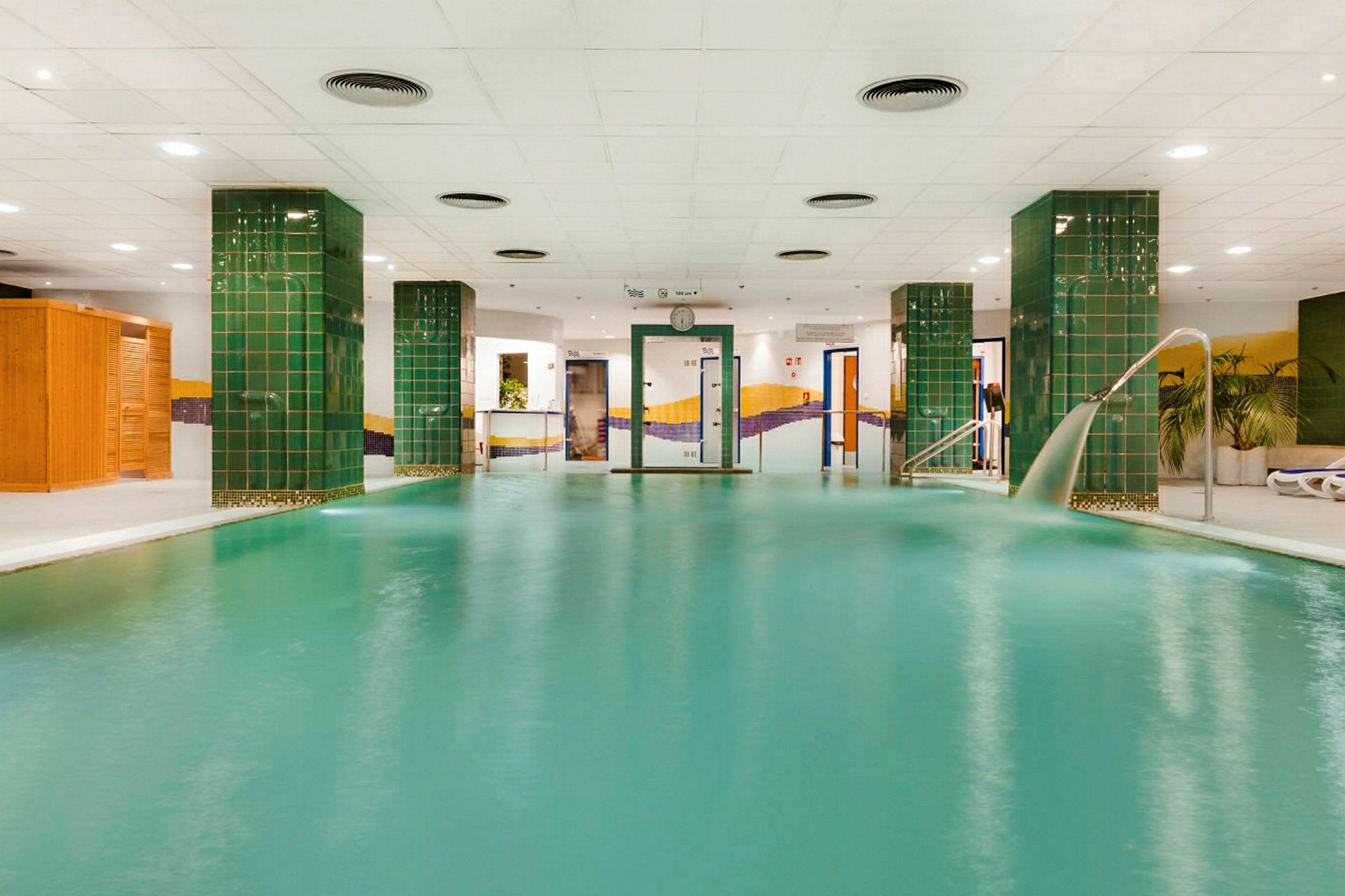 En inomhuspool med gröna pelare och vitt tak. (AI-genererad text)
