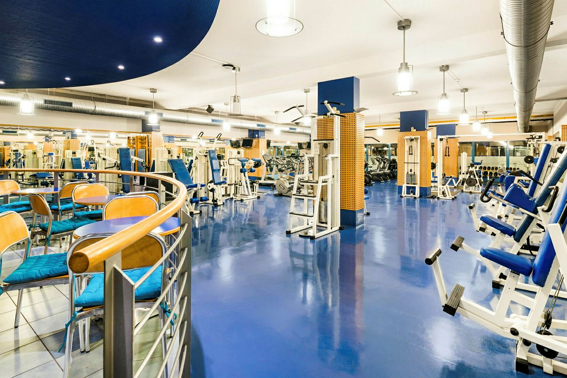 Ett modernt gym med träningsutrustning och bord med stolar i förgrunden. (AI-genererad text)