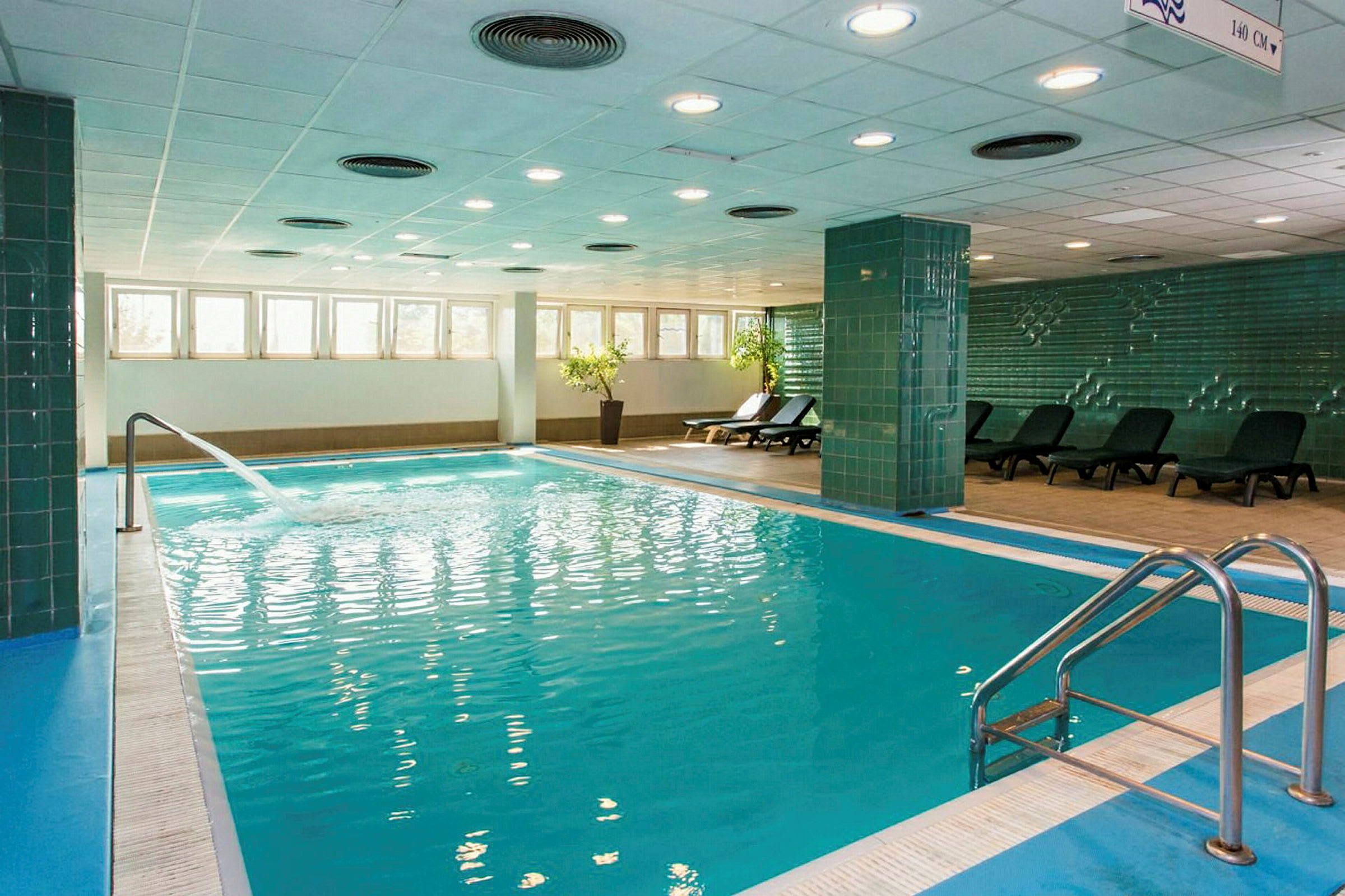 Inomhuspool med solstolar vid sidan och en fontän som flödar in i vattnet. (AI-genererad text)