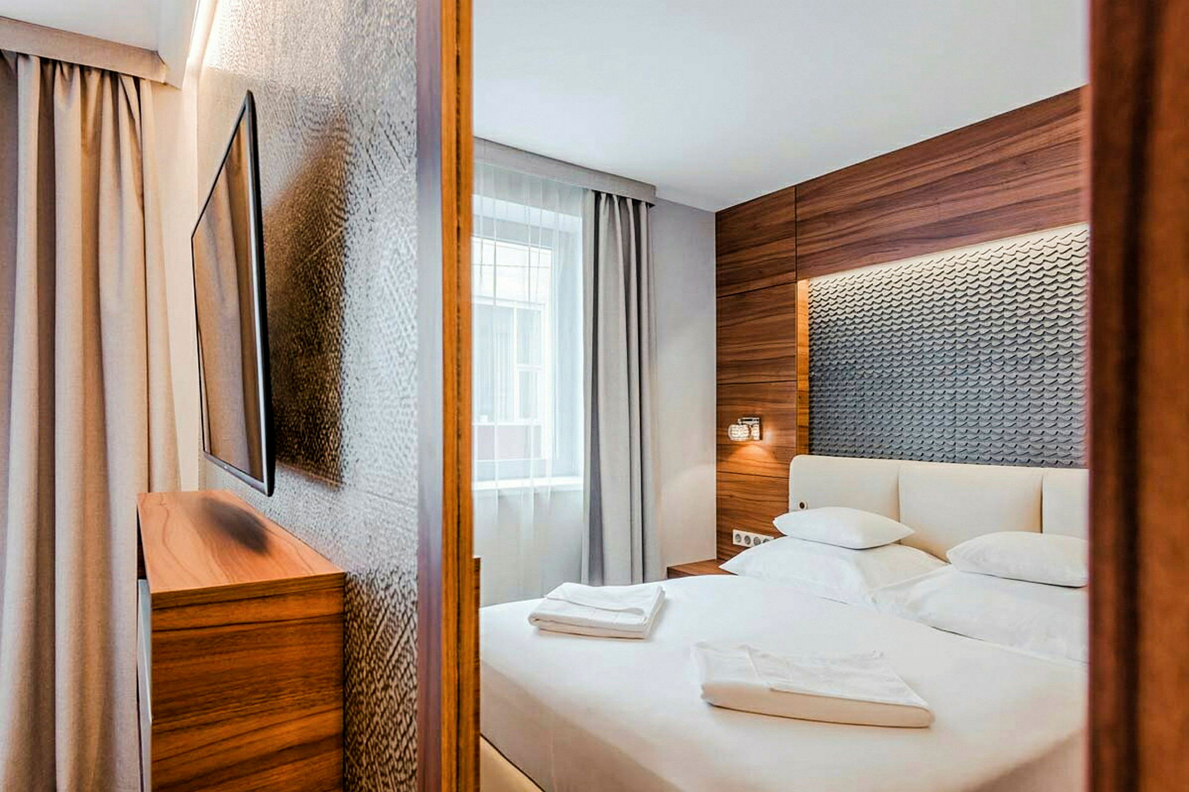 Ett modernt hotellrum med en stor säng, dekorerat med träpaneler och texturerad vägg bakom sänggaveln. (AI-genererad text)