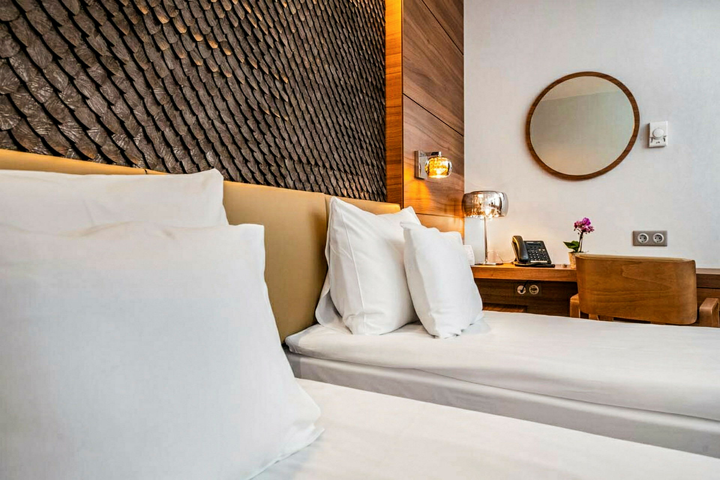 Ett hotellrum med två enkelsängar, ett träskrivbord med stol, en telefon, och en runda spegel på väggen. (AI-genererad text)