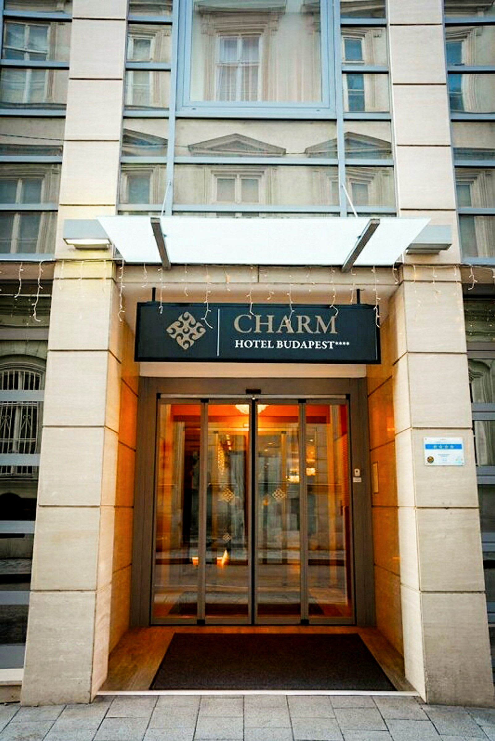 Entrén till Charm Hotel Budapest med skylt och glasdörrar. (AI-genererad text)