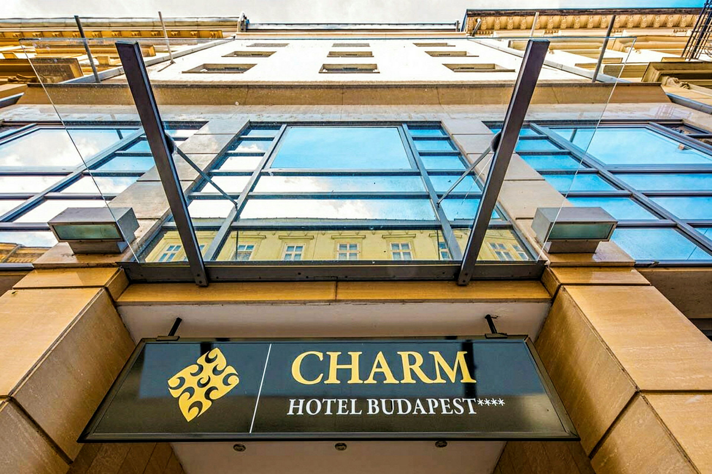 Fasadbild av en byggnad med ett skylt som visar namnet "CHARM Hotel Budapest****". (AI-genererad text)