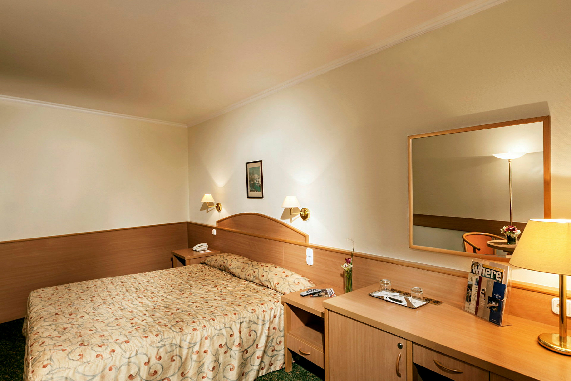 Hotellrum med dubbelsäng, nattduksbord, spegel och skrivbord. (AI-genererad text)