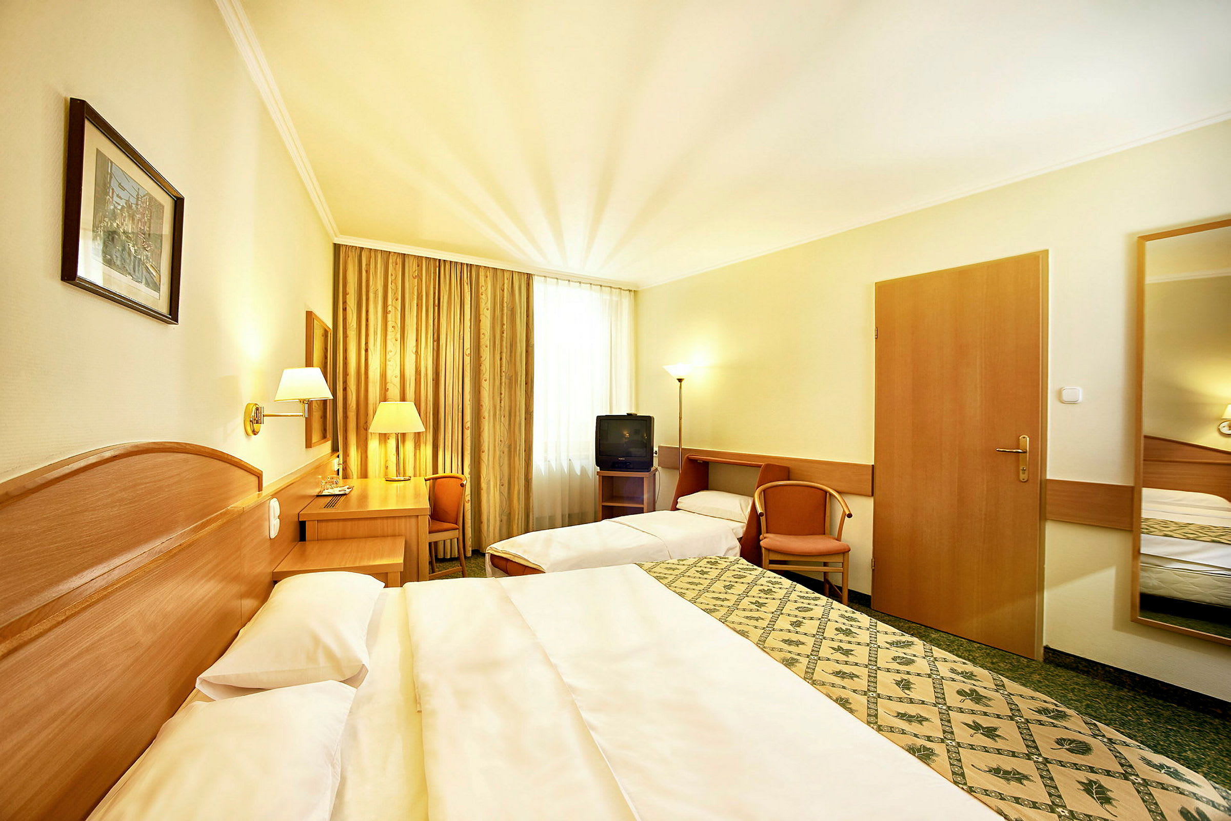 Ett hotellrum med två sängar, en skrivbordshörna och ett fönster med gardiner. (AI-genererad text)