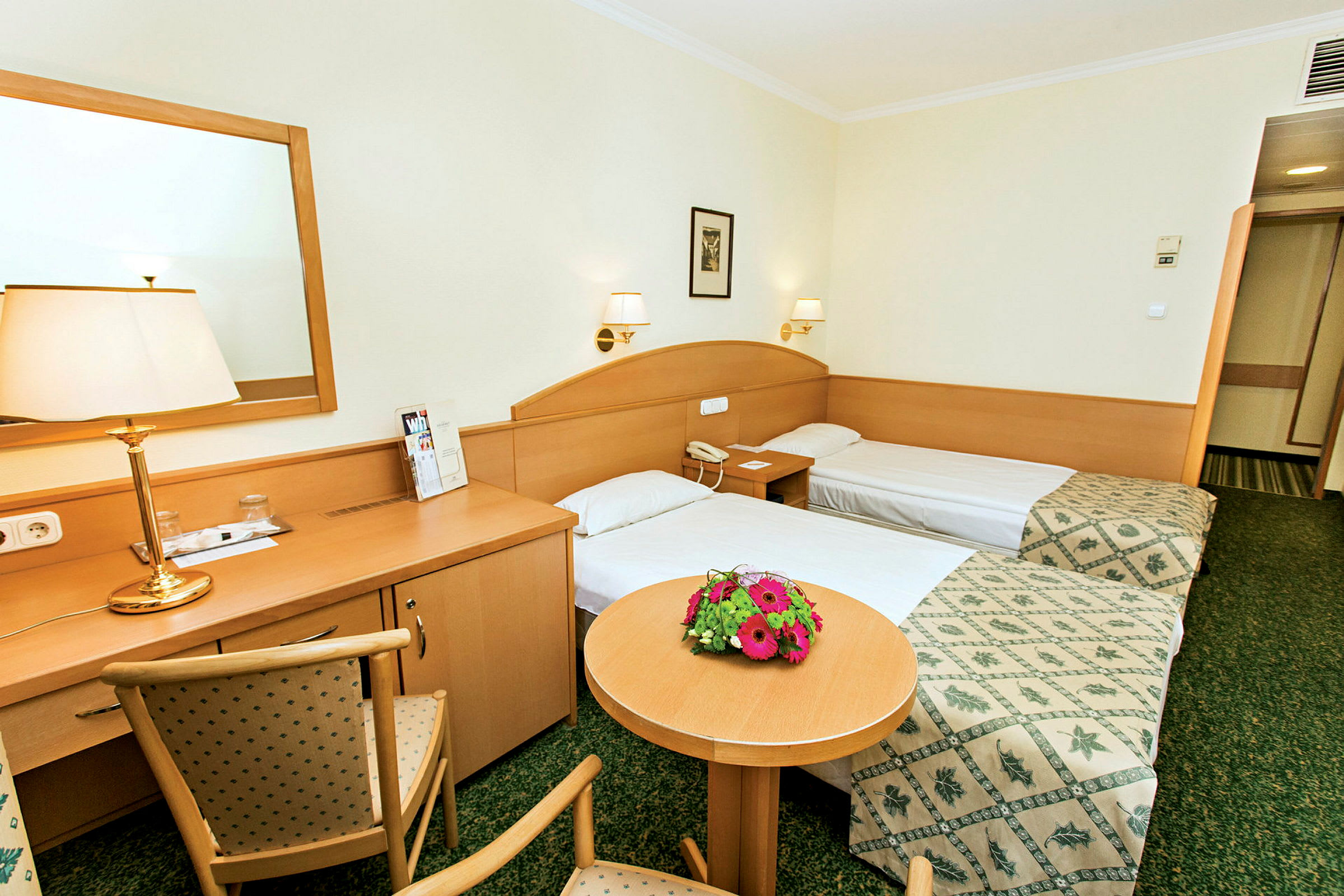 Två enkelsängar i ett hotellrum med träinredning och blommor på ett bord. (AI-genererad text)