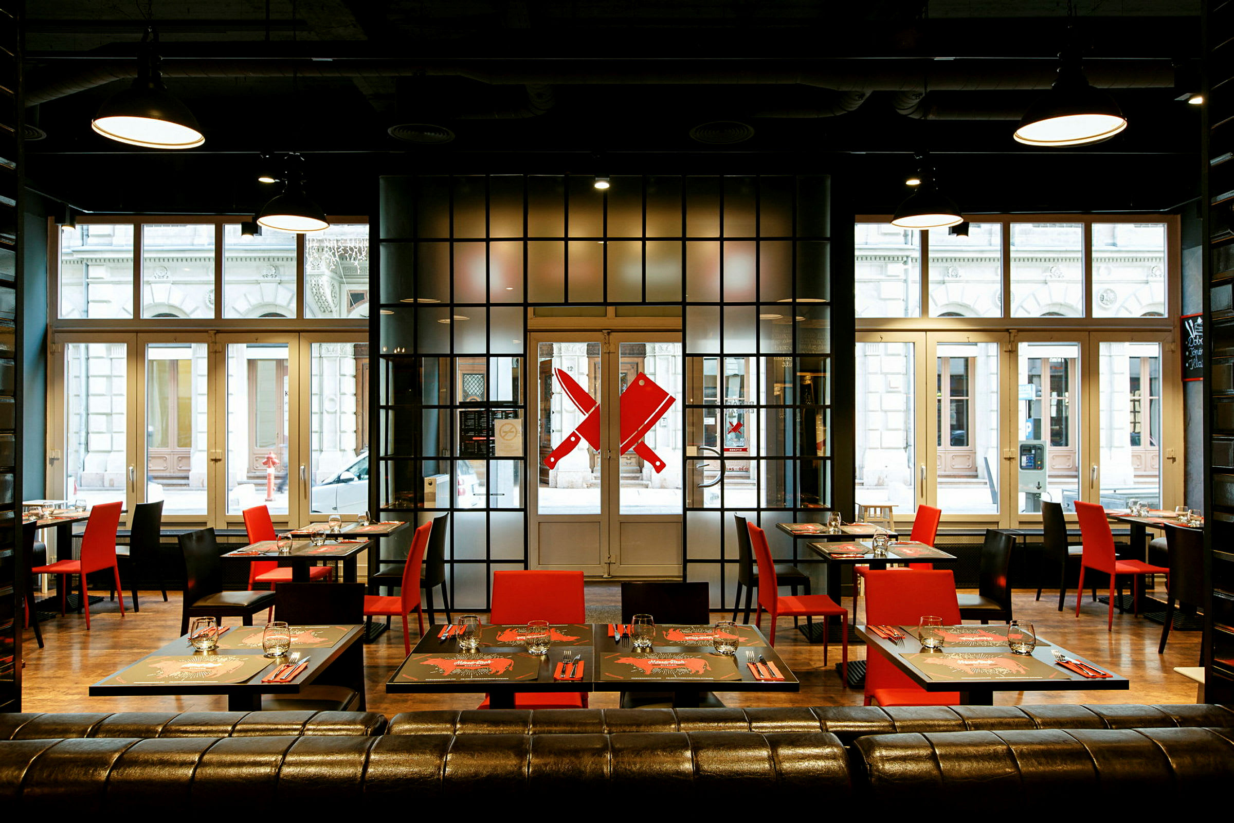 Modern restaurang med röda och svarta stolar samt dukade bord framför stora fönster. (AI-genererad text)