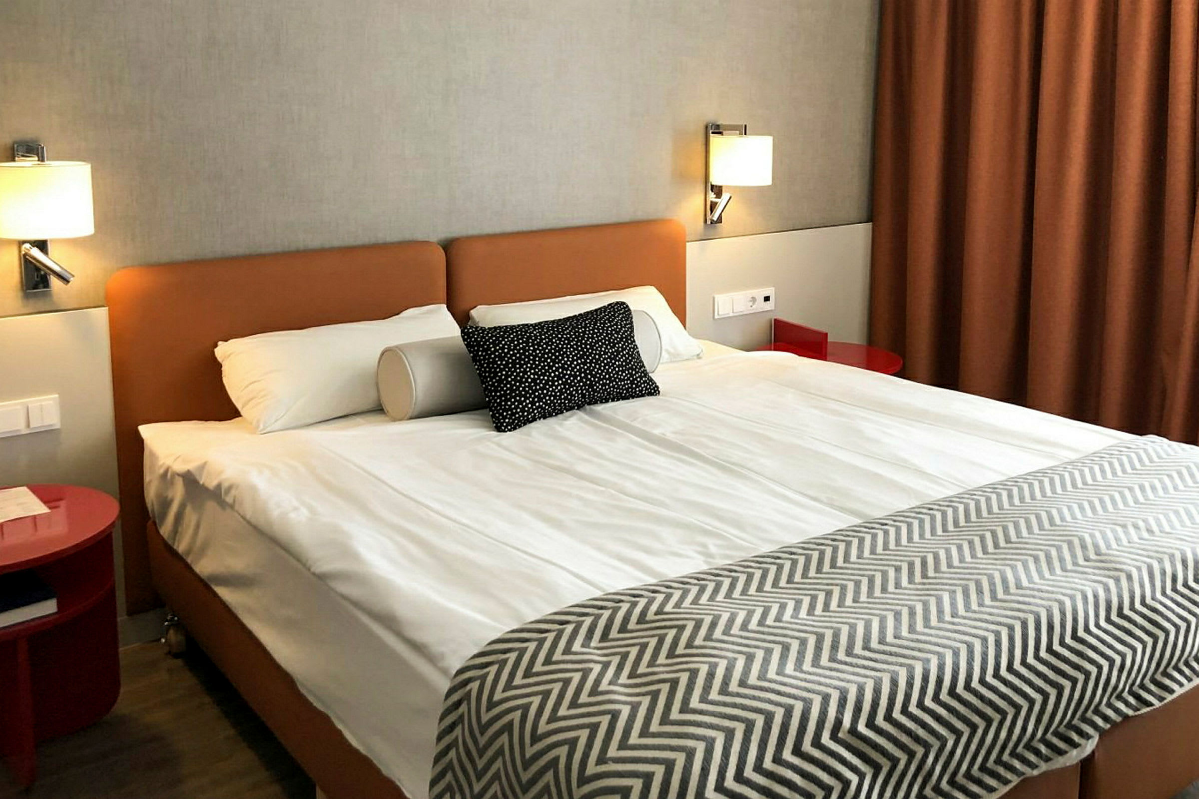Ett hotellrum med en dubbelsäng, litet sängbord och en brun gardin. (AI-genererad text)