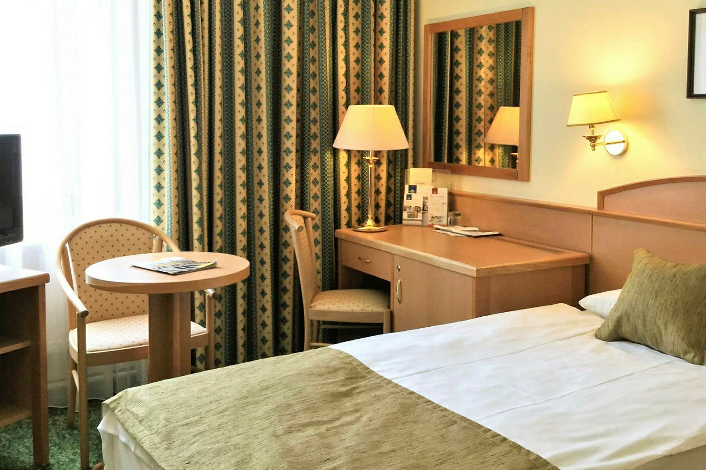 Hotellrum med säng, skrivbord och sittplats vid ett litet bord. (AI-genererad text)