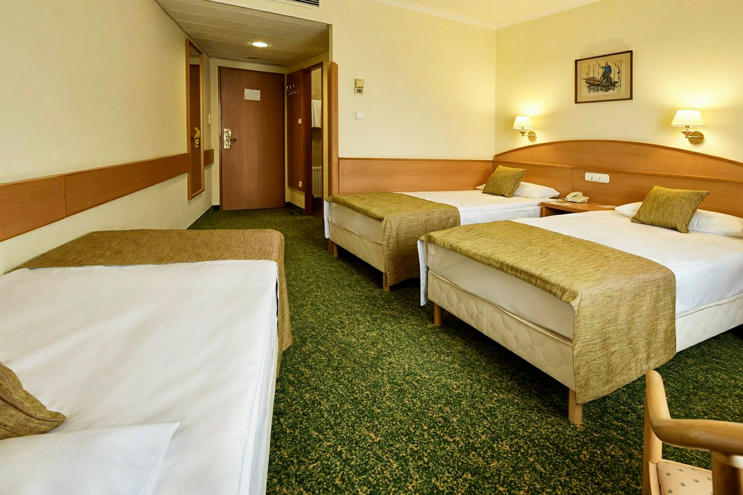 Hotellrum med tre enkelsängar, gröna sängöverkast och ljusa väggar. (AI-genererad text)