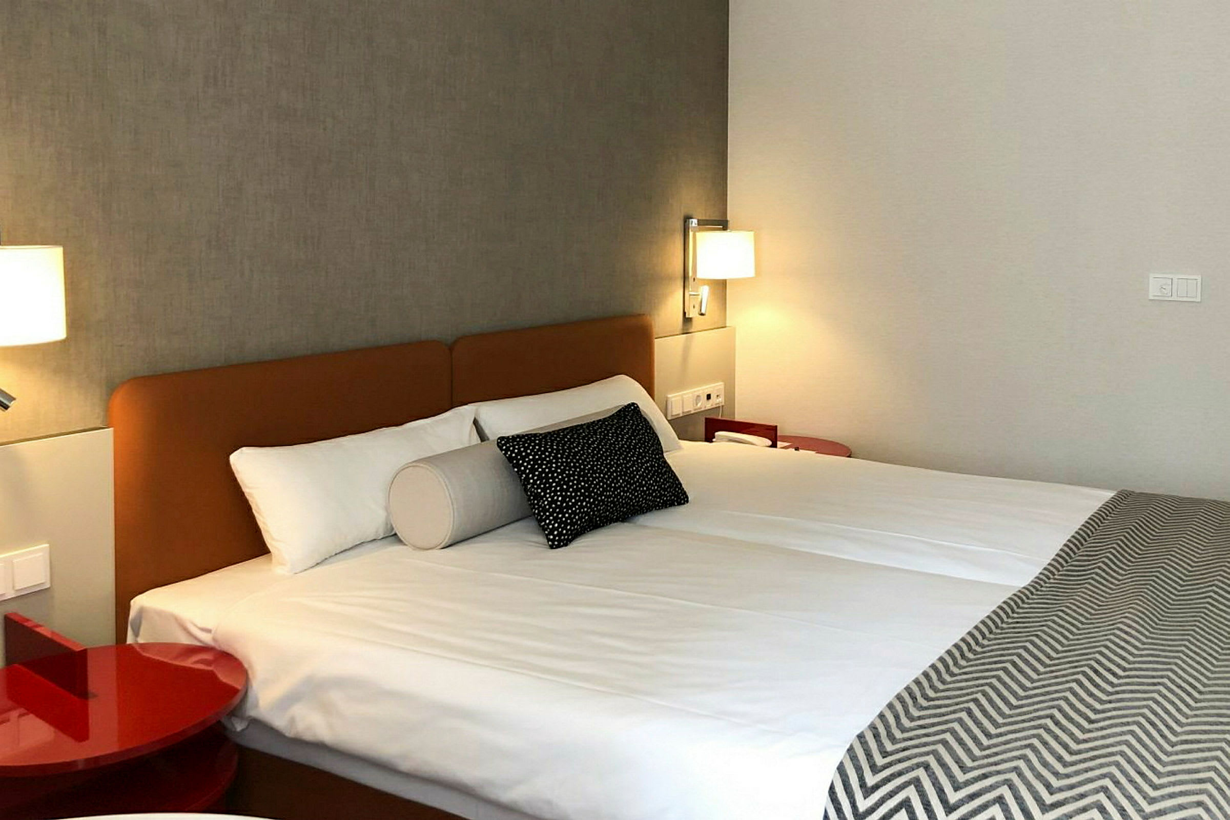 Ett hotellrum med en dubbelsäng, upplyst med vägglampor. (AI-genererad text)