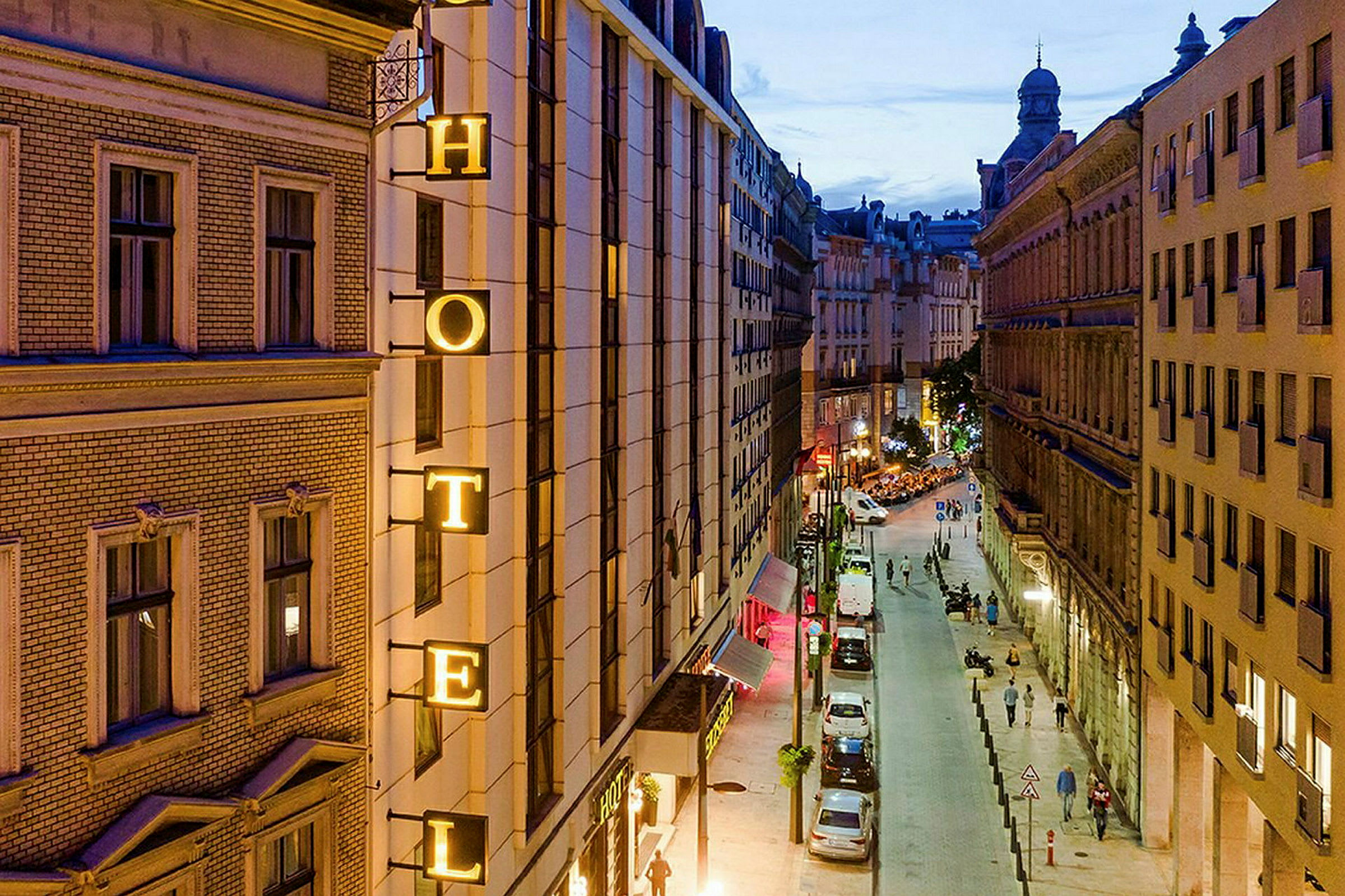 Bild av en stadsgata på kvällen med en hotellskylt på en byggnad. (AI-genererad text)