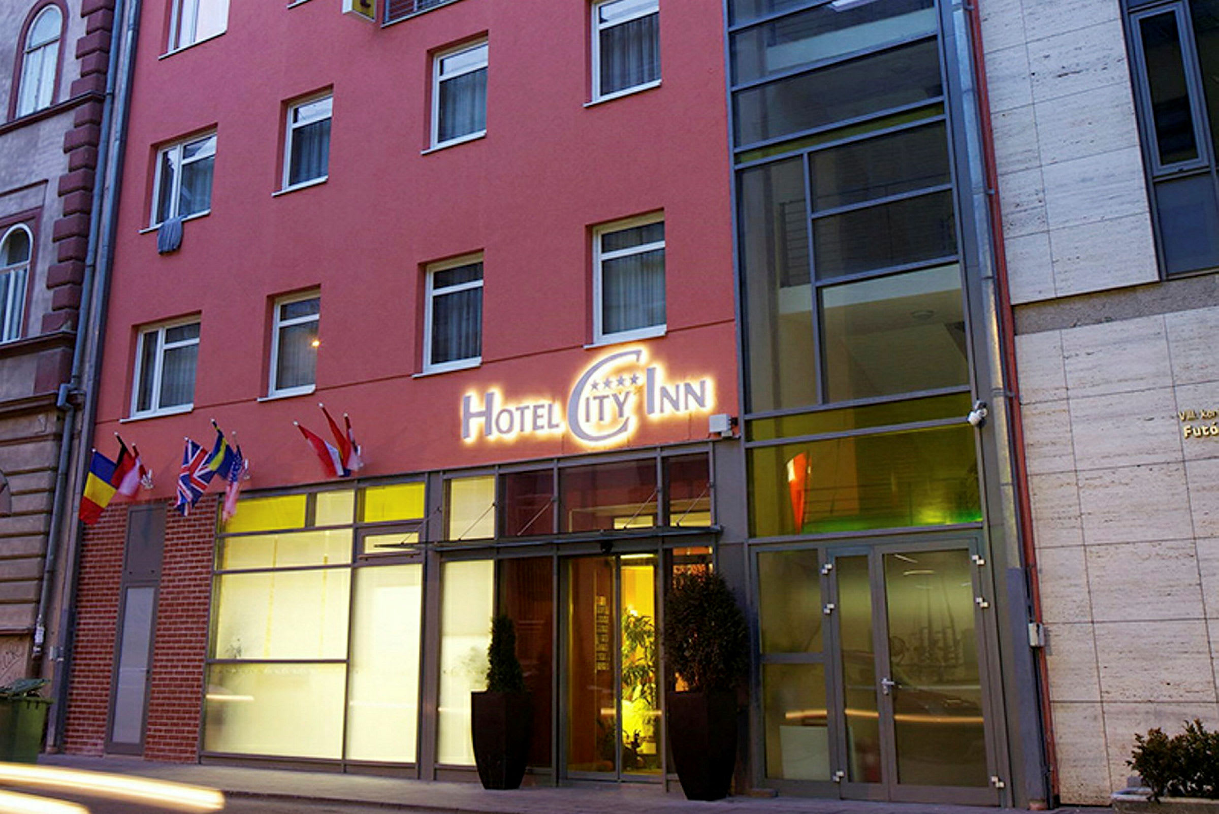 Utanför en hotellbyggnad med en skylt som lyder "Hotel City Inn" samt flera flaggor vid entrén. (AI-genererad text)